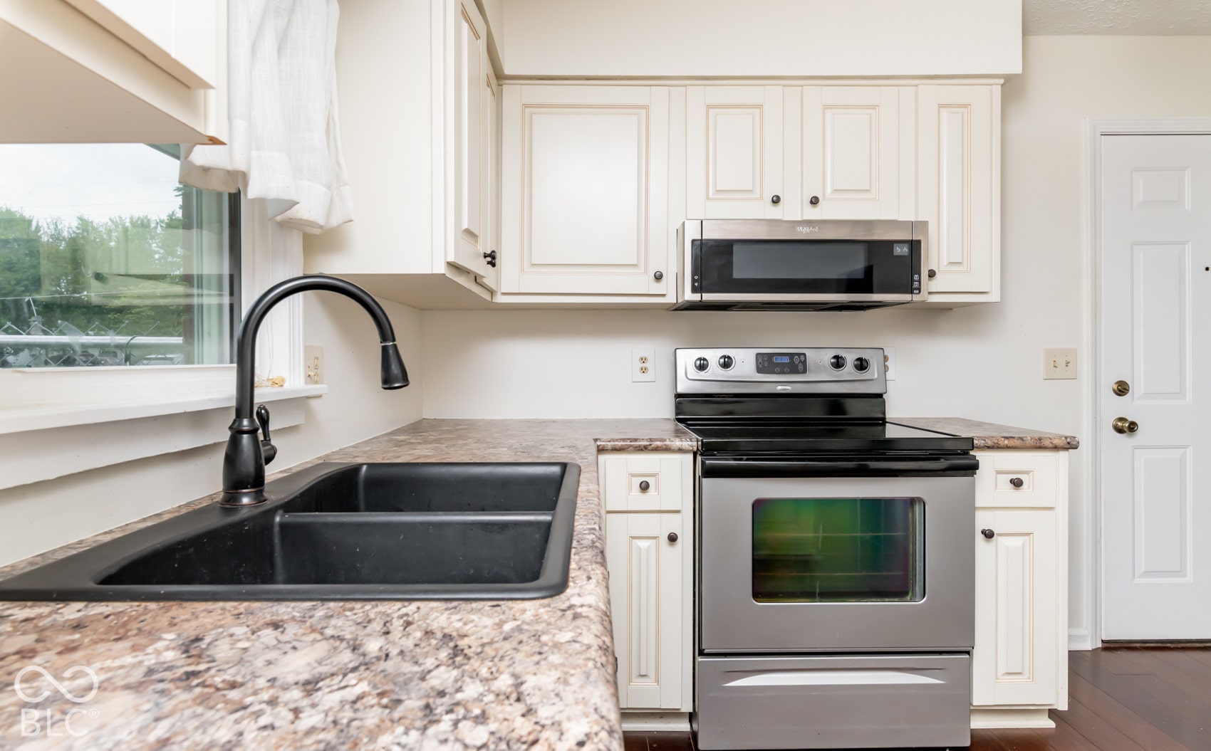 White cabinetry, stainless steel appliances, black double basin sink, and a contrasting countertop