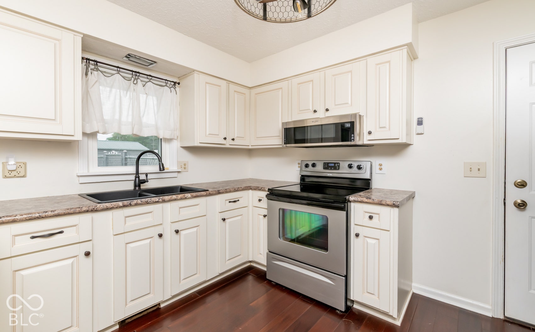 Kitchen featuring white cabinetry, dark-finish countertops, stainless steel appliances, and wood-finish flooring