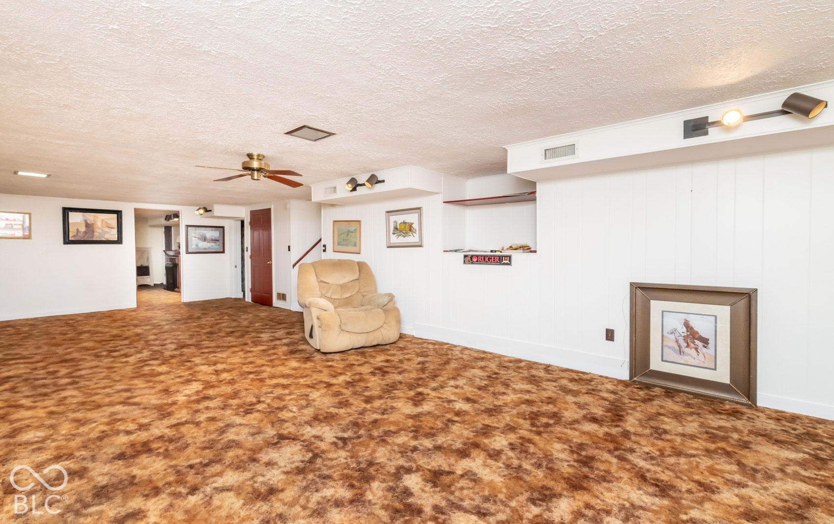 Expansive room with textured carpet flooring, white painted walls, ceiling fan, and track lighting