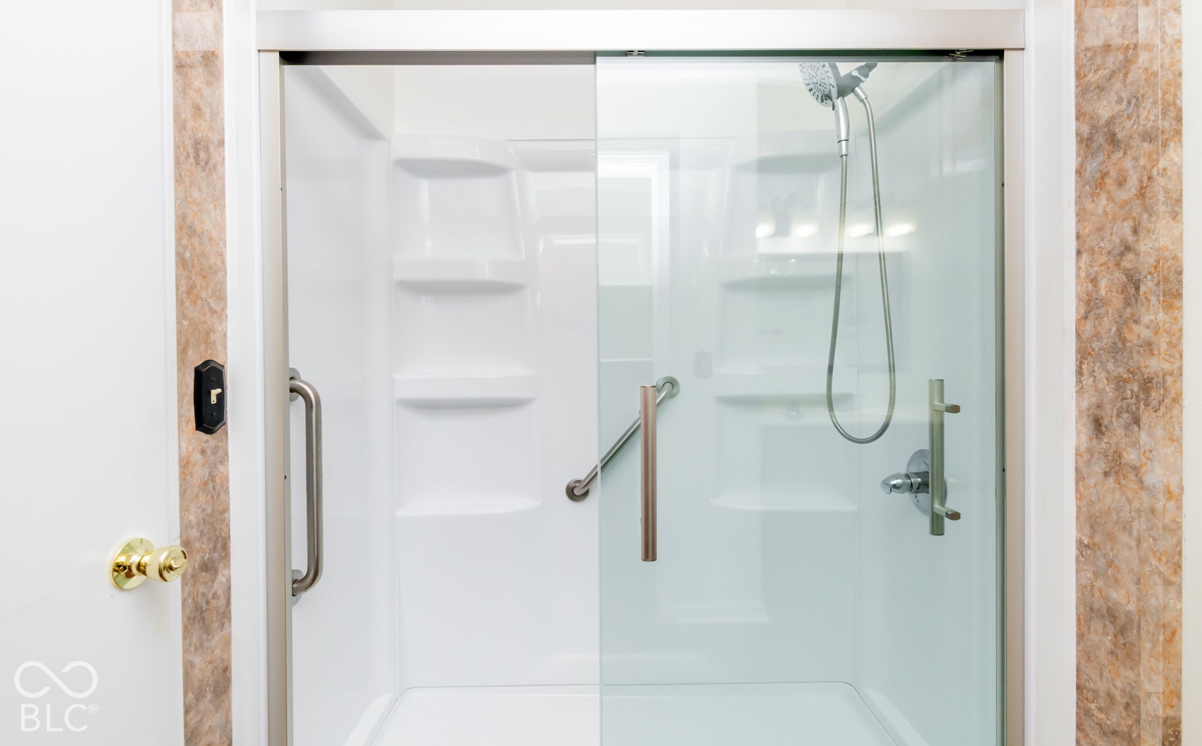 Sliding glass shower enclosure with white composite surround, integrated shelving, and a handheld showerhead