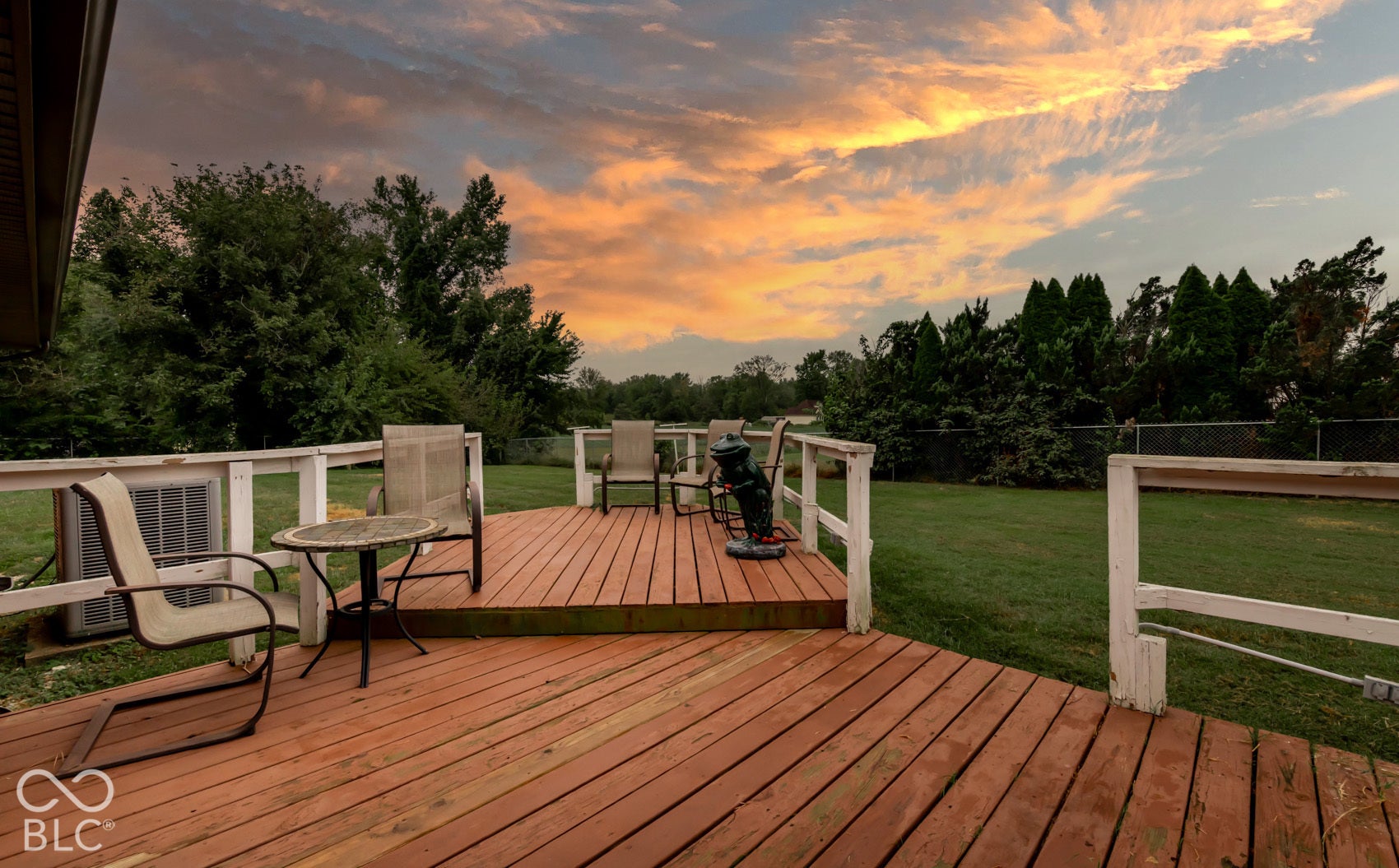 Expansive wood deck with a white railing, overlooking a large green lawn and mature trees