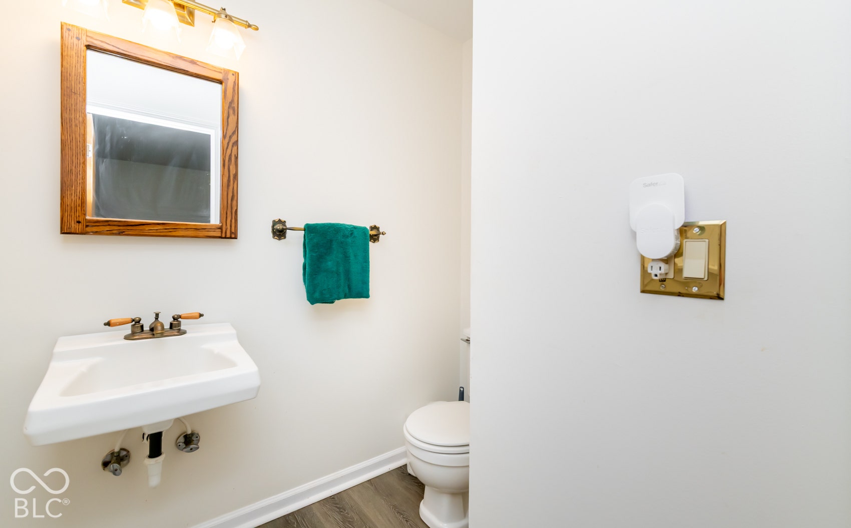 Wall-mounted sink with brass-finish faucet, wood-framed mirror, and overhead vanity lighting