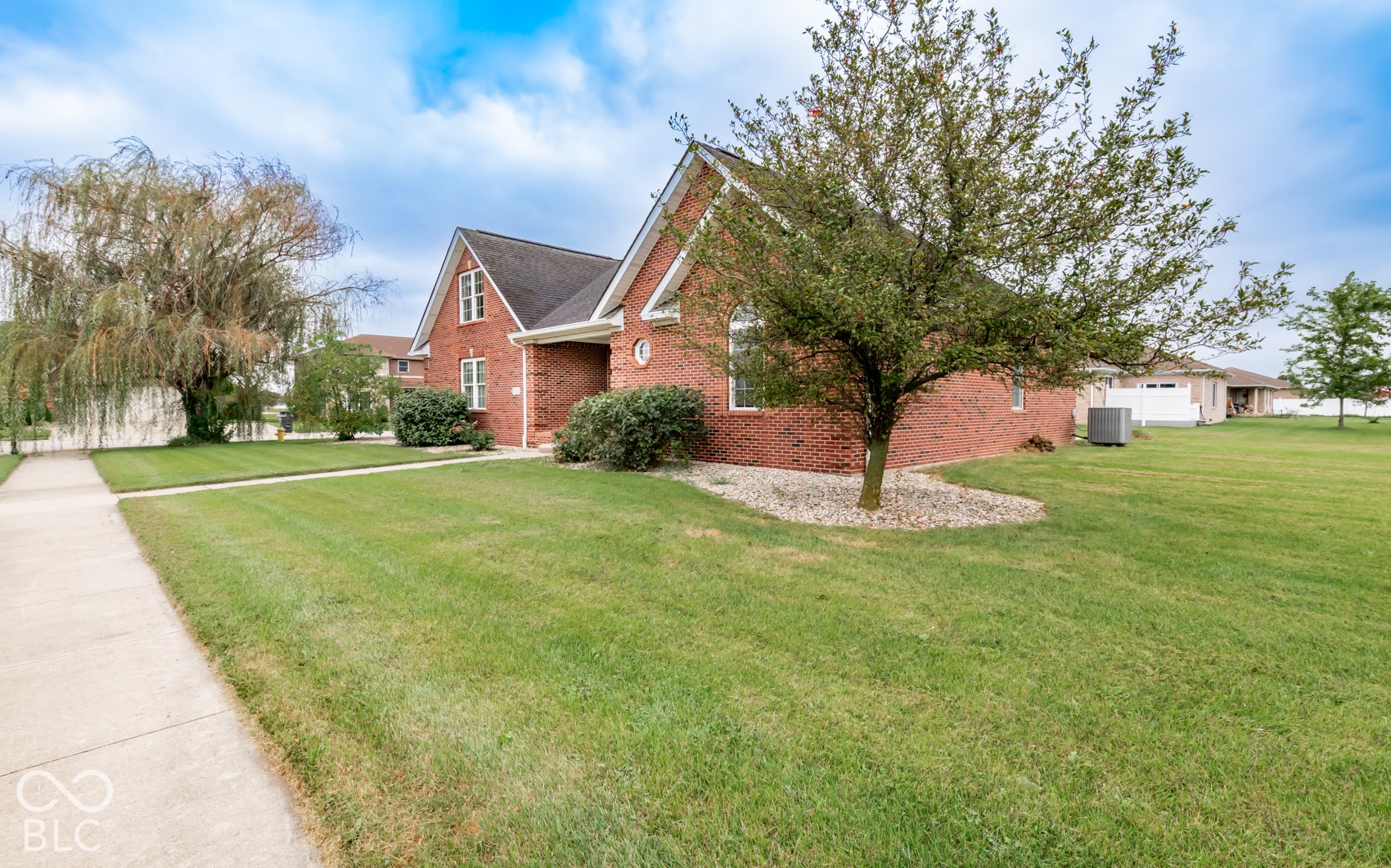 Brick exterior, gabled roofline, mature trees, expansive lawn, concrete sidewalk