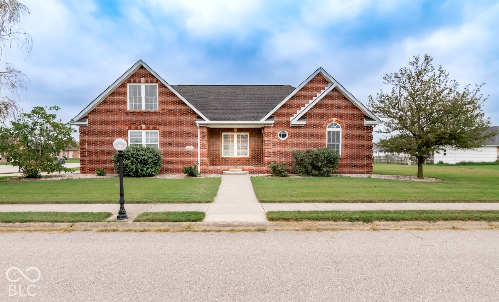 Red brick exterior with a dark shingle roof, symmetrical gables, and a concrete walkway