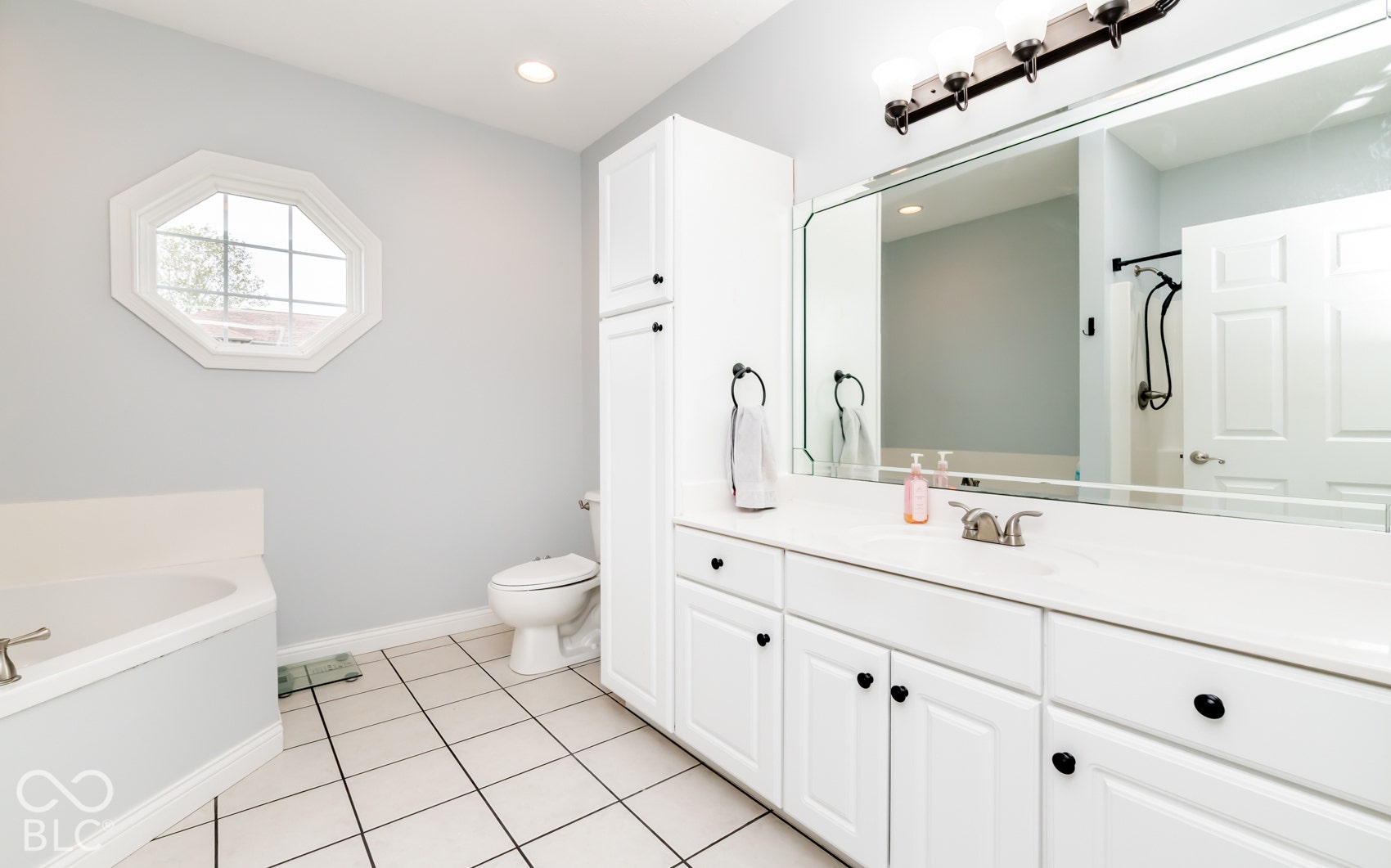 White tile flooring complemented by a corner soaking tub and an octagonal window