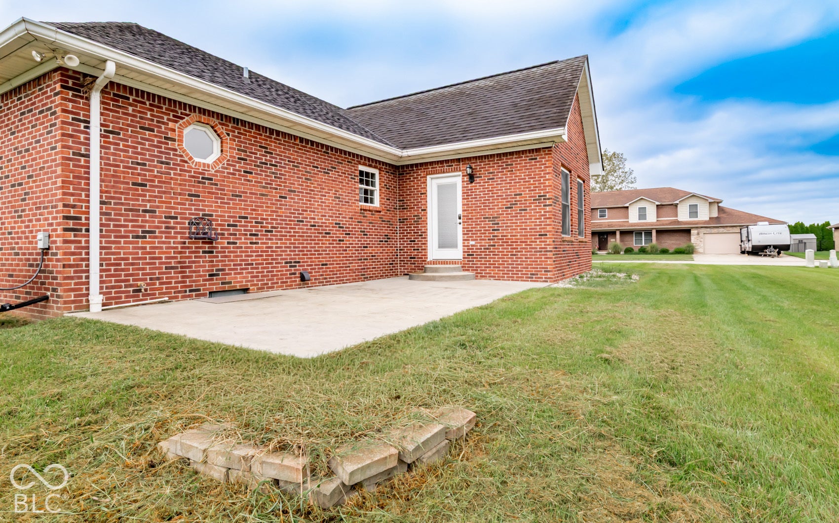 Brick exterior with white trim, concrete patio, white door, and a circular window