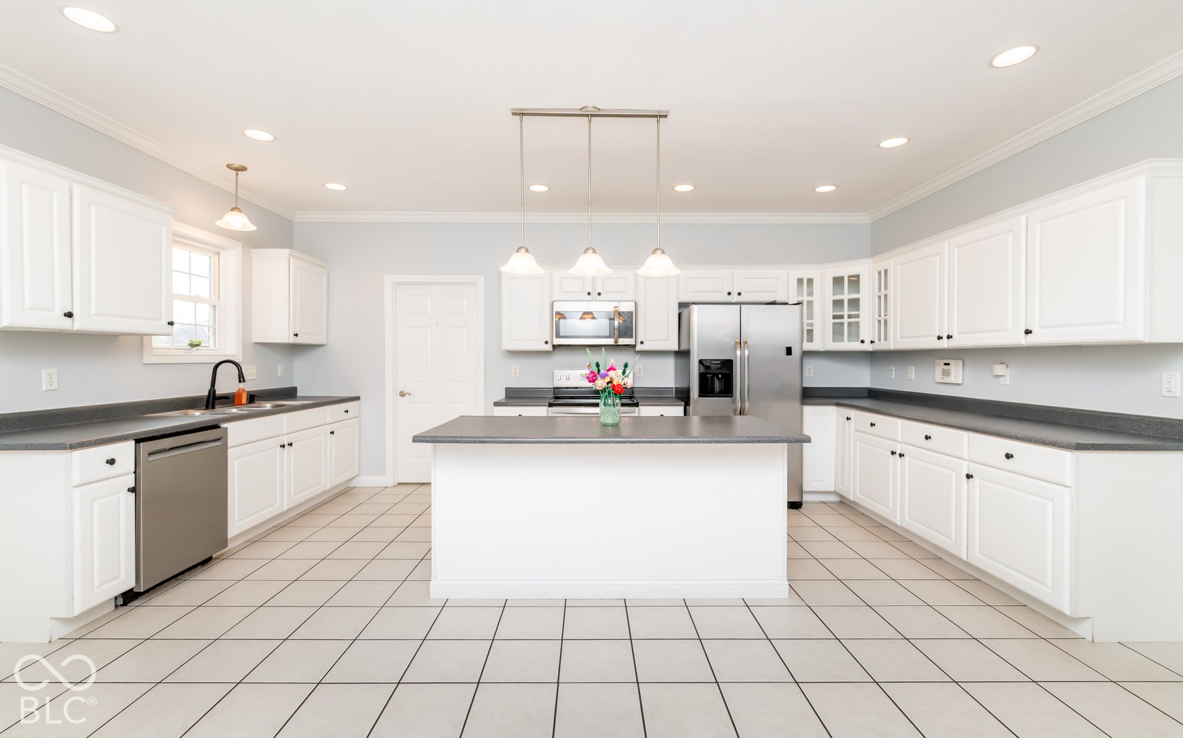 White shaker-style cabinetry, stainless steel appliances, central island, tiled flooring, and recessed lighting