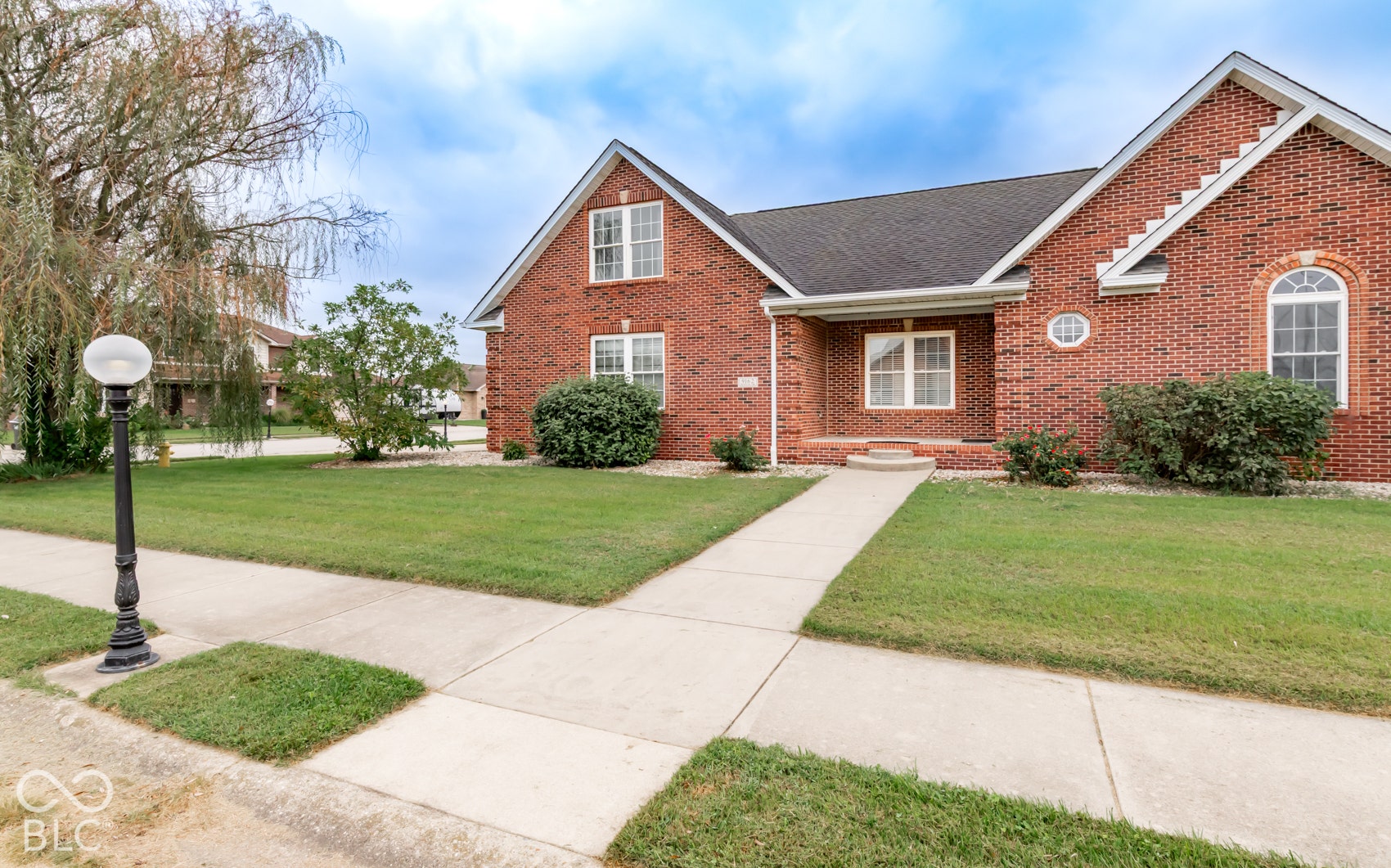 Brick exterior with decorative brickwork, arched window, covered entry, front walkway, and manicured lawn