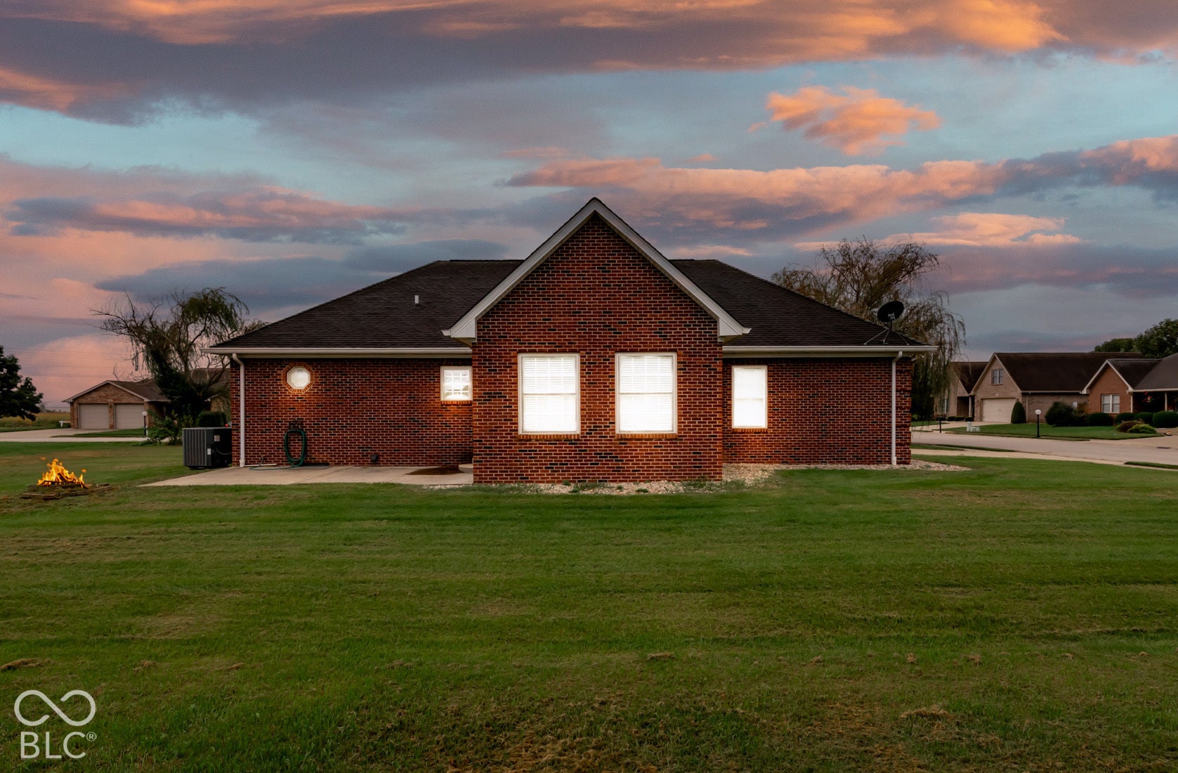 Brick exterior with white-framed windows, dark shingle roof, and a flat concrete patio