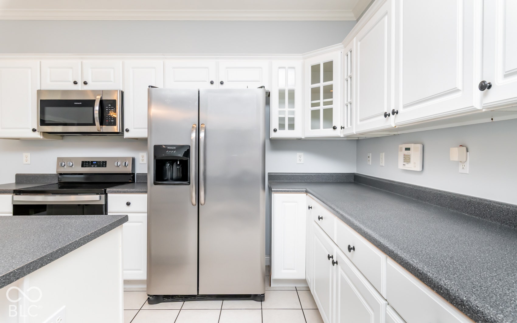 White shaker-style cabinetry, stainless steel appliances, dark textured countertops, and tile flooring