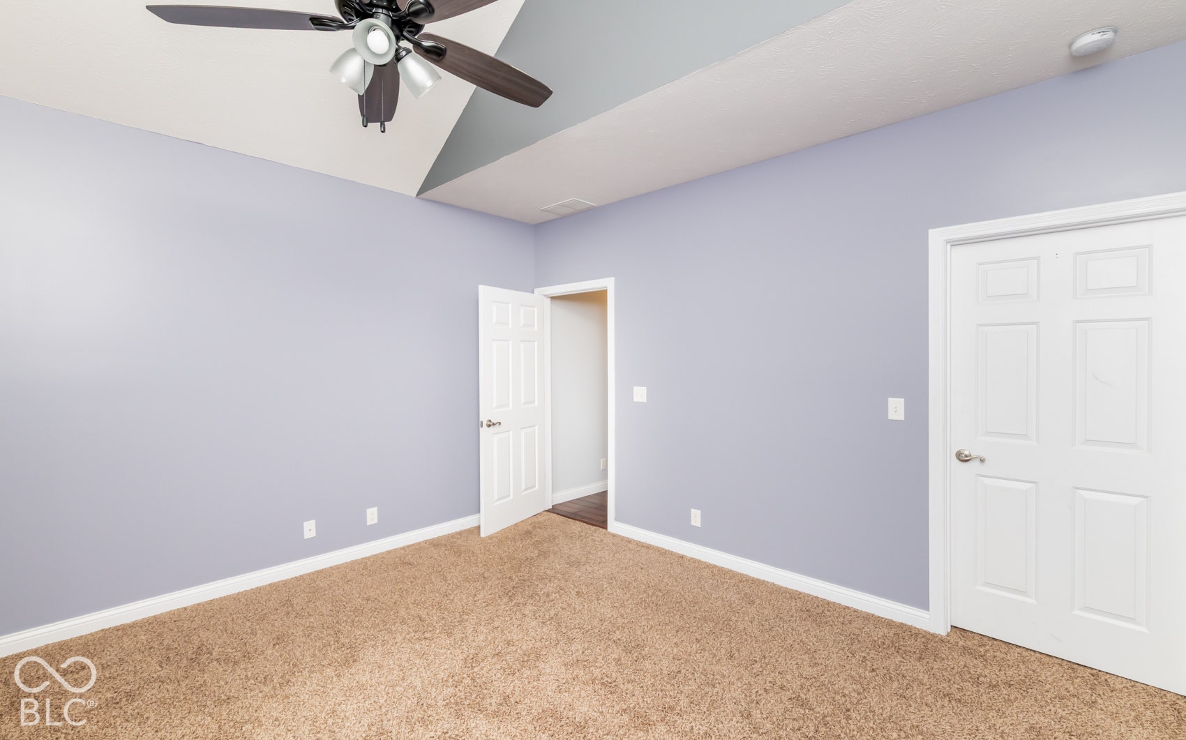 Vaulted ceiling with a ceiling fan, light lavender walls, and neutral carpet flooring