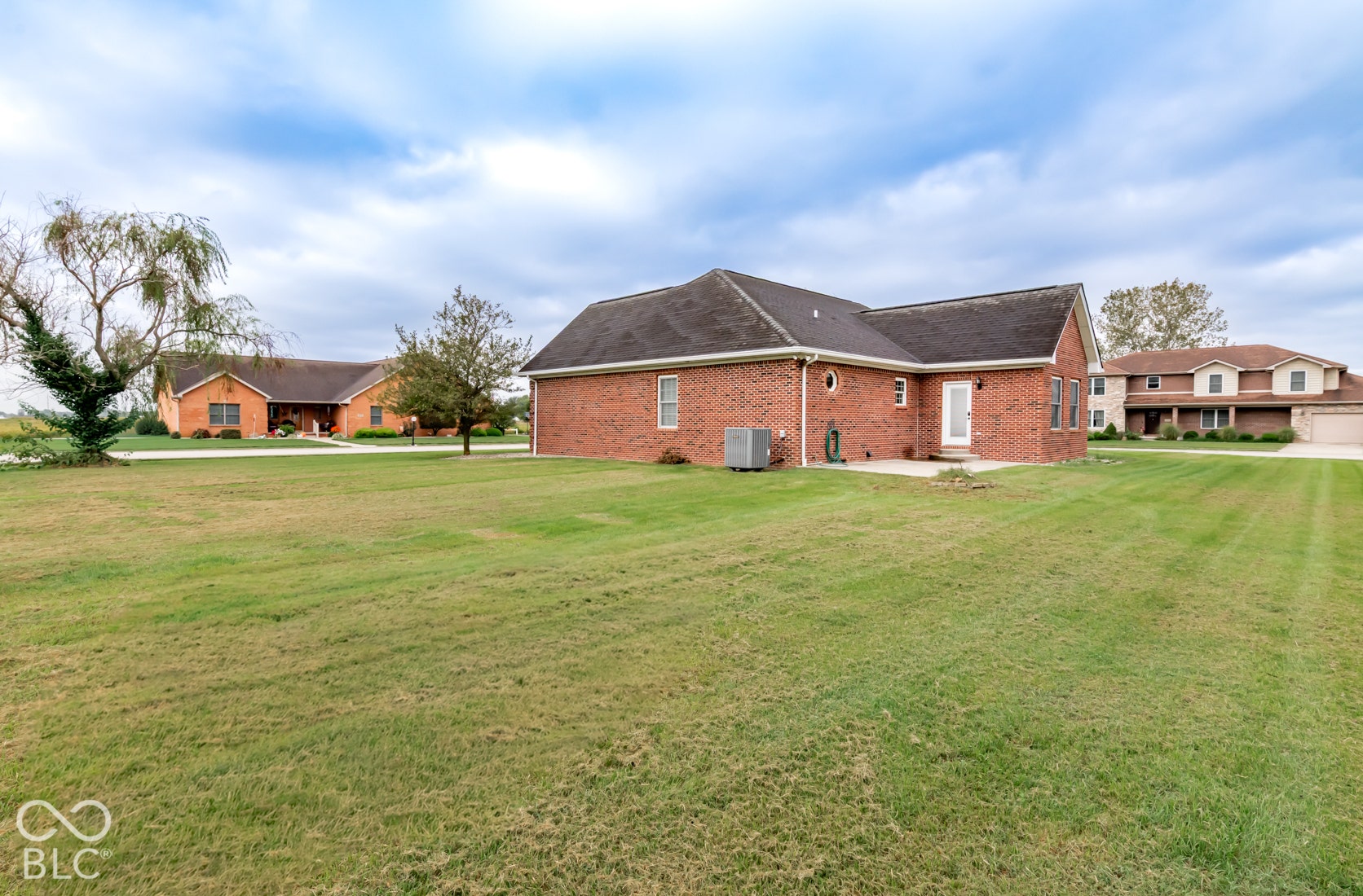 Expansive green lawn with a brick exterior home and a paved patio