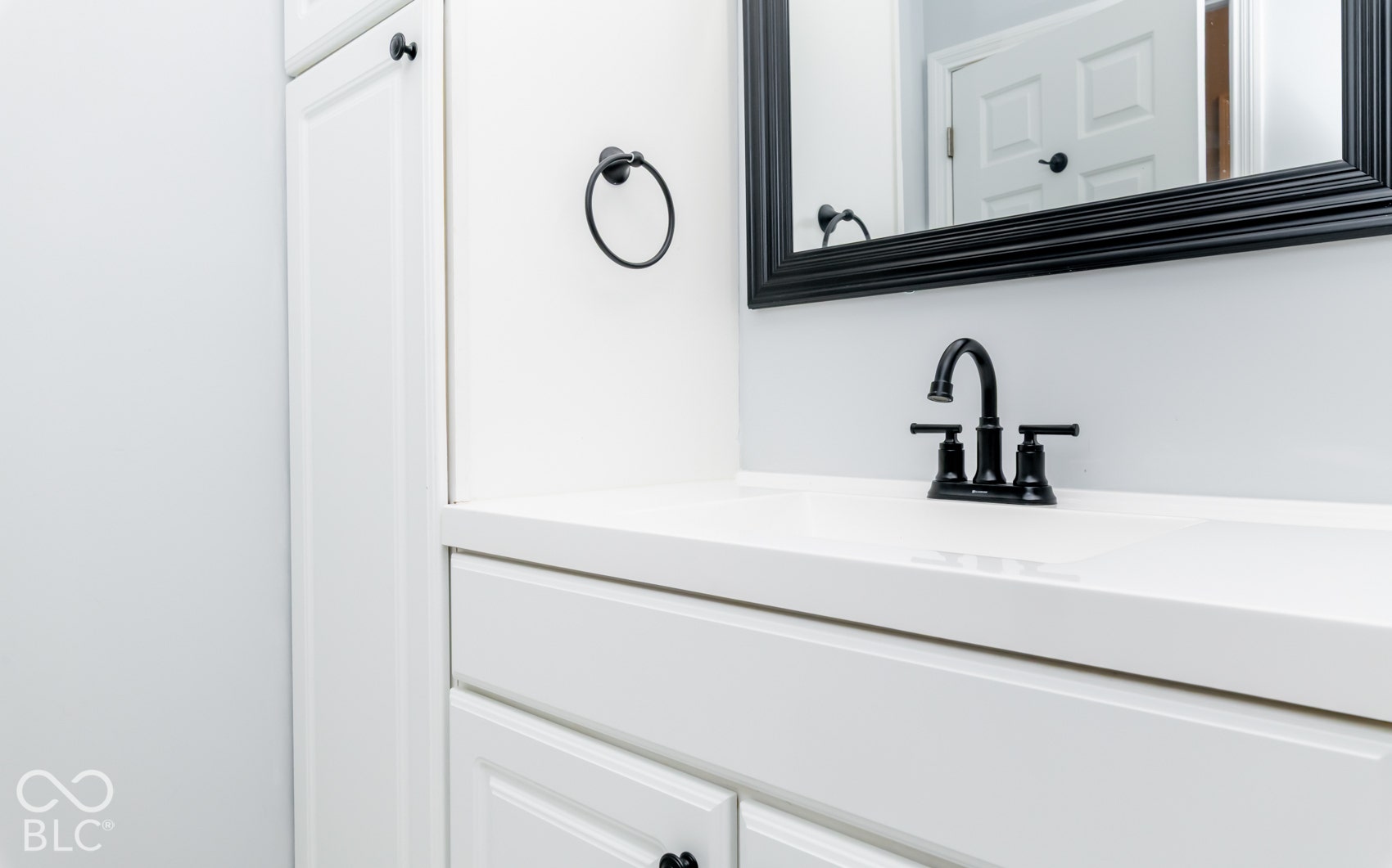 White vanity with a solid surface countertop, matte black faucet, and framed mirror