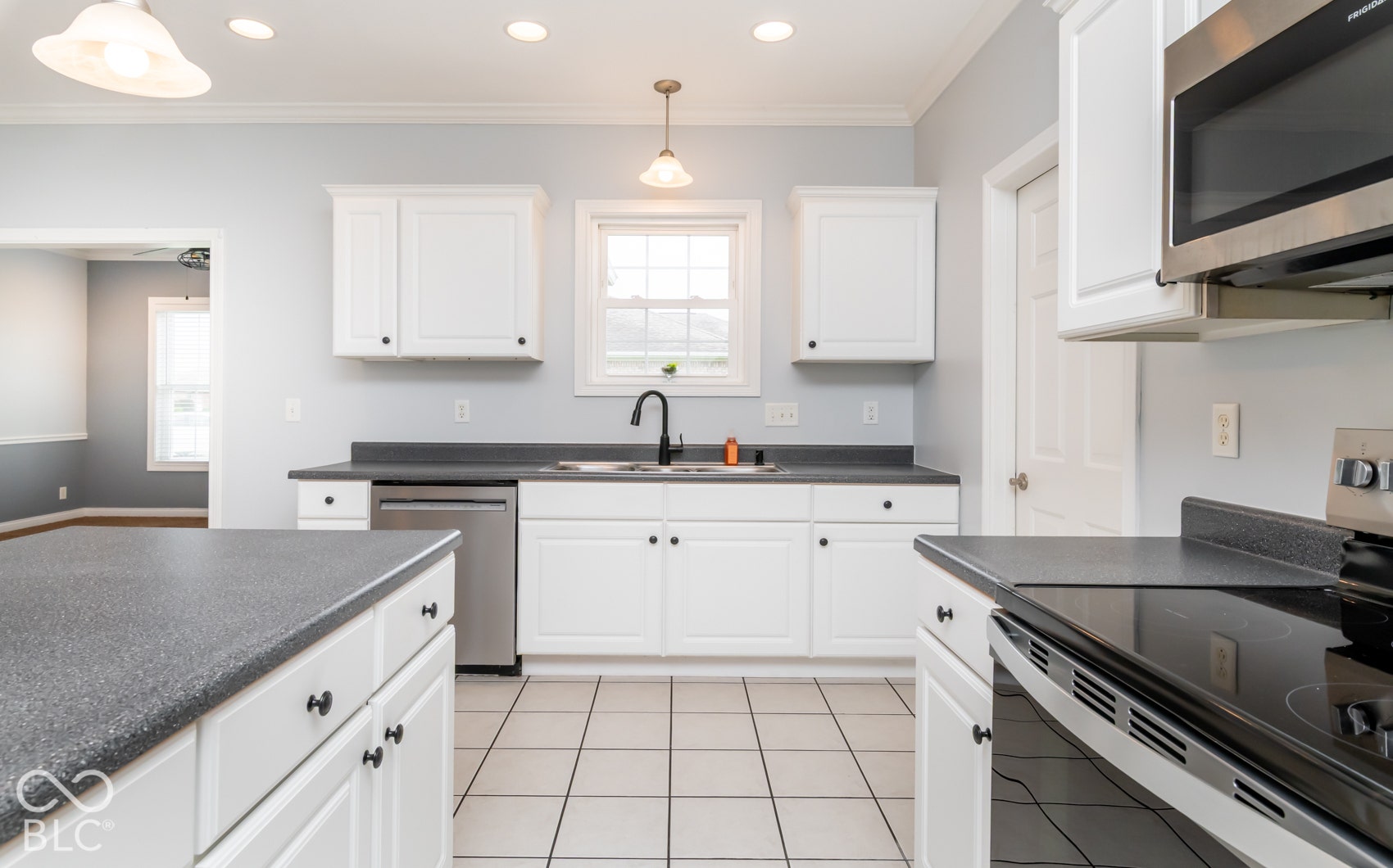 Kitchen featuring white cabinetry, dark countertops, a stainless steel dishwasher, an over-range microwave, and tile flooring