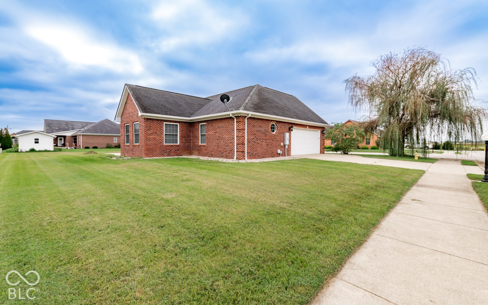 Brick exterior with white trim, attached garage, well-maintained lawn, and a concrete sidewalk