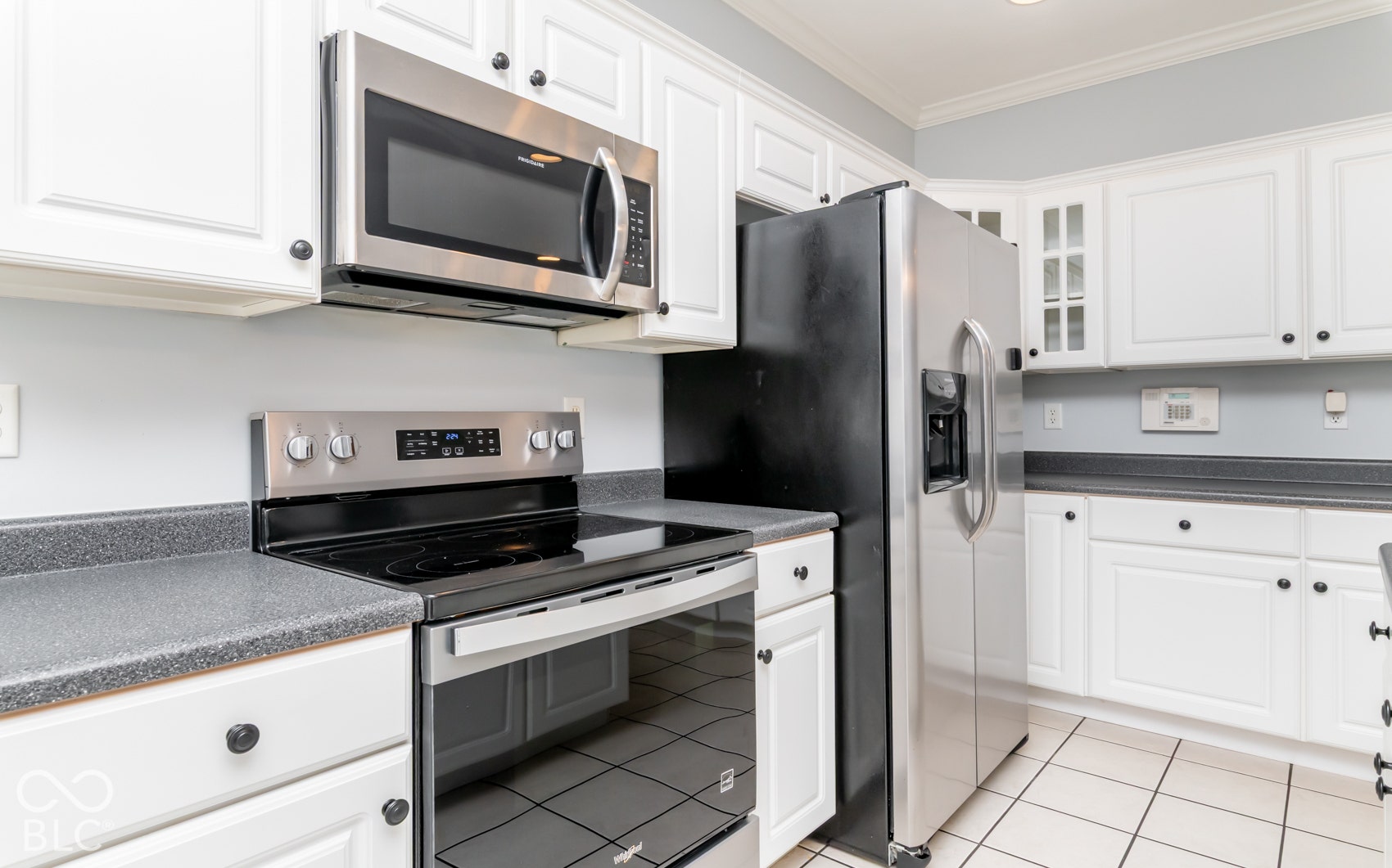 White shaker-style cabinetry with black hardware, stainless steel appliances, solid surface countertops, and white tile flooring