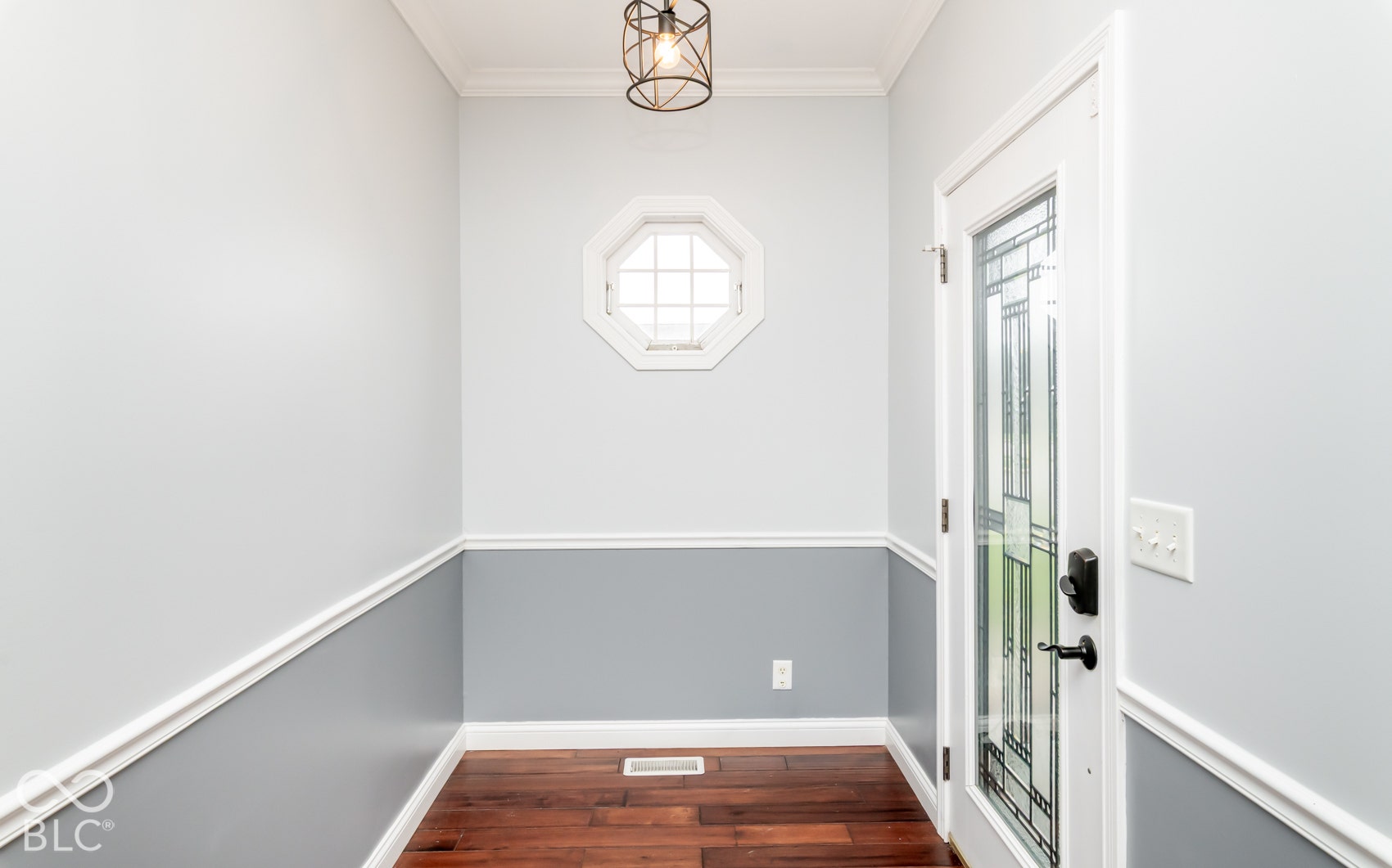 Hardwood-finish flooring, two-tone wall treatment, decorative chair rail, octagonal transom window, and a door with frosted glass paneling