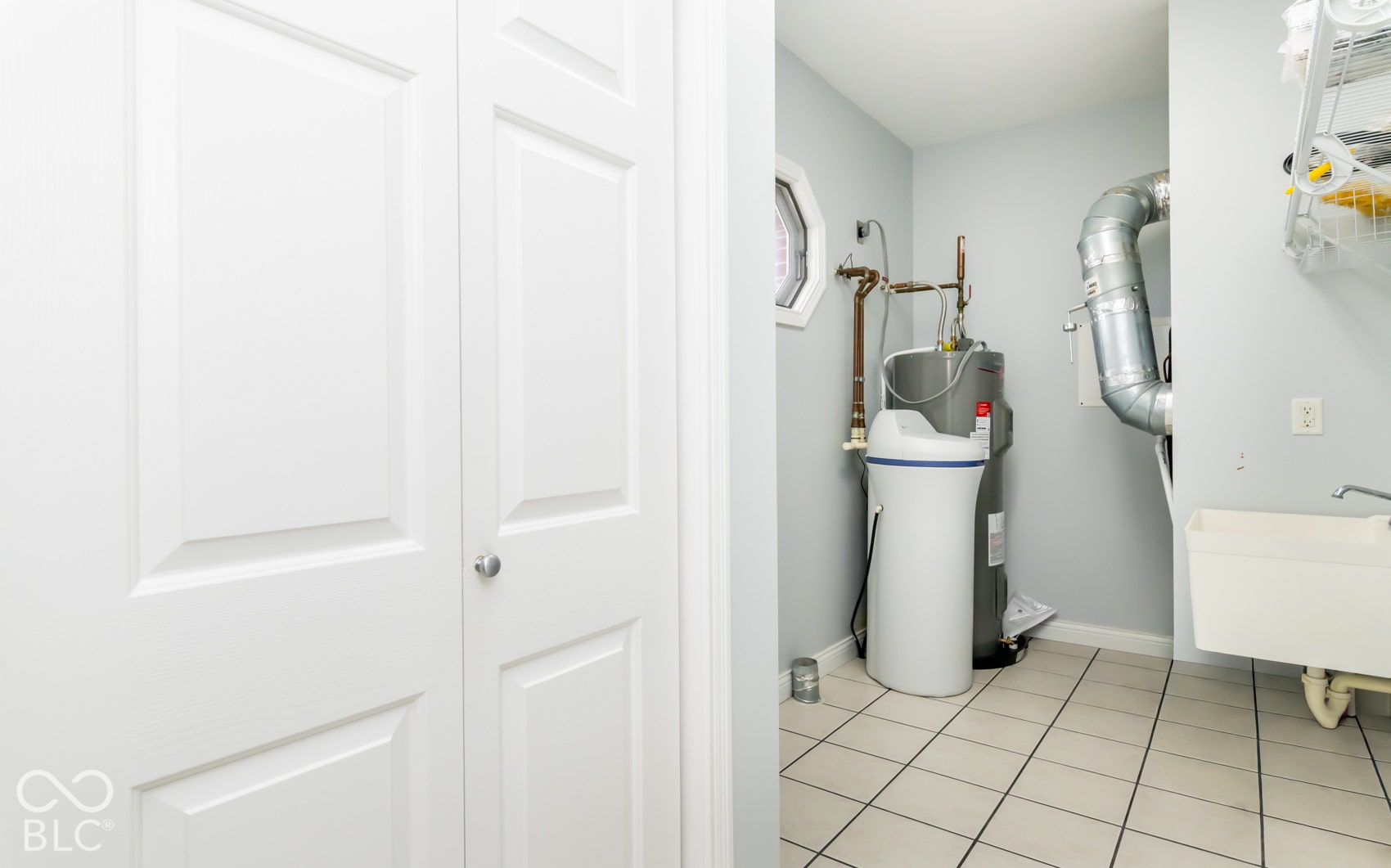 Utility area featuring tiled flooring, a water heater, a water softener system, a utility sink, and an octagonal window
