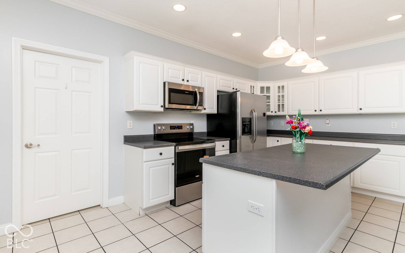 White cabinetry, stainless steel appliances, dark countertops, kitchen island, and recessed lighting