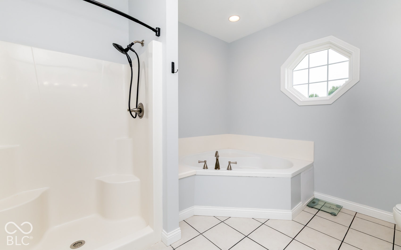 Walk-in shower with curved rod, corner soaking tub with deck-mounted faucet, octagonal window, recessed ceiling light, and tiled flooring
