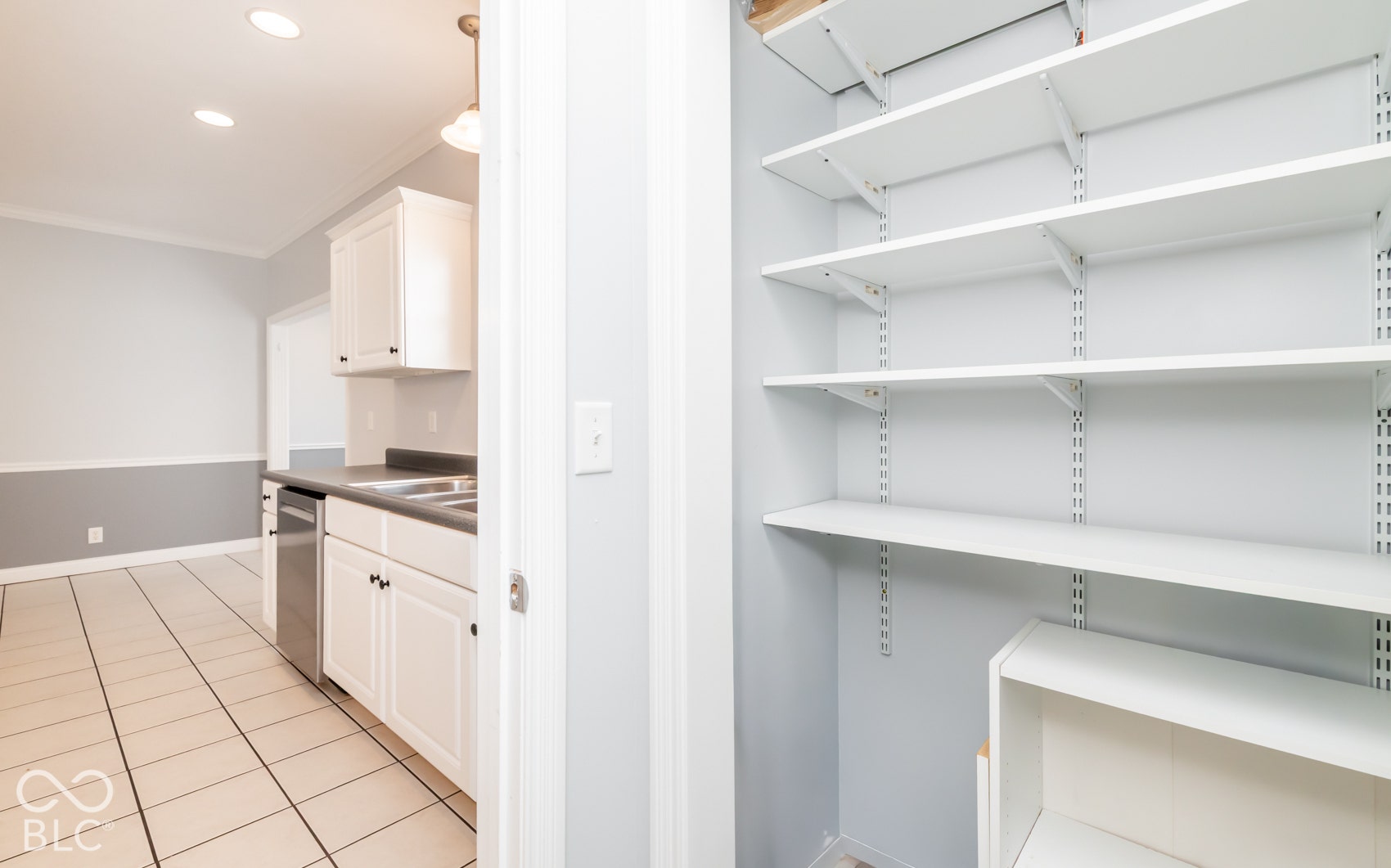 Adjustable shelving system, recessed ceiling lighting, white cabinetry, integrated stainless steel dishwasher, and tile flooring