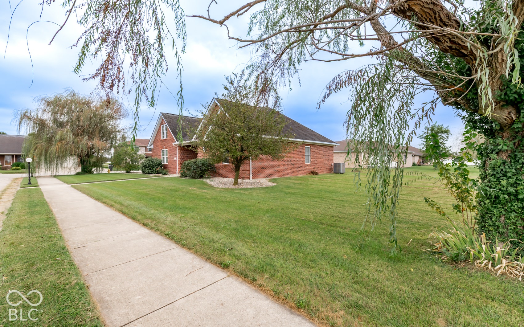 Brick exterior with white trim, green lawn, established trees, and a concrete sidewalk