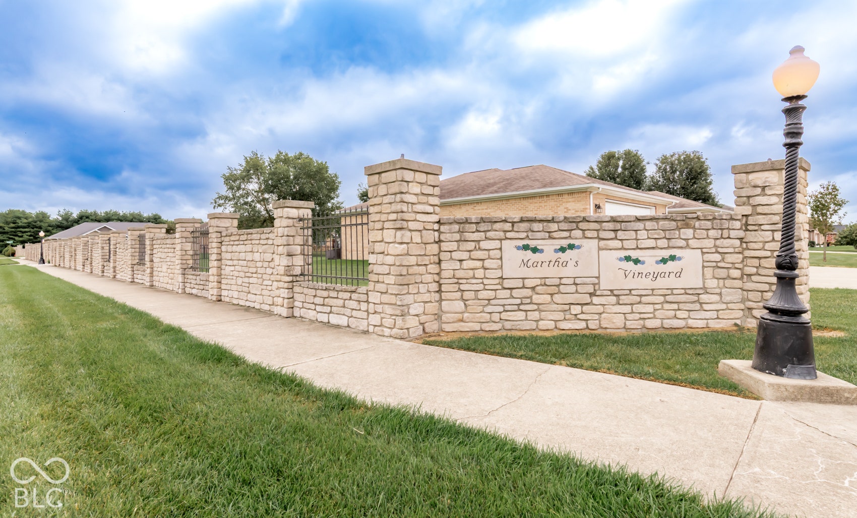 Stone veneer wall with decorative iron fencing, a stone veneer pillar, and a black ornamental street lamp