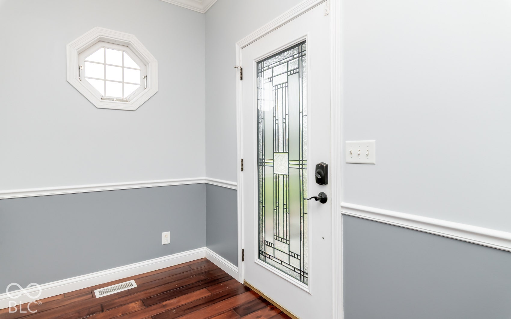 Entryway featuring a decorative octagon window, wood-finish flooring, two-tone wall treatment with chair rail, crown molding, and a front door with leaded glass insert