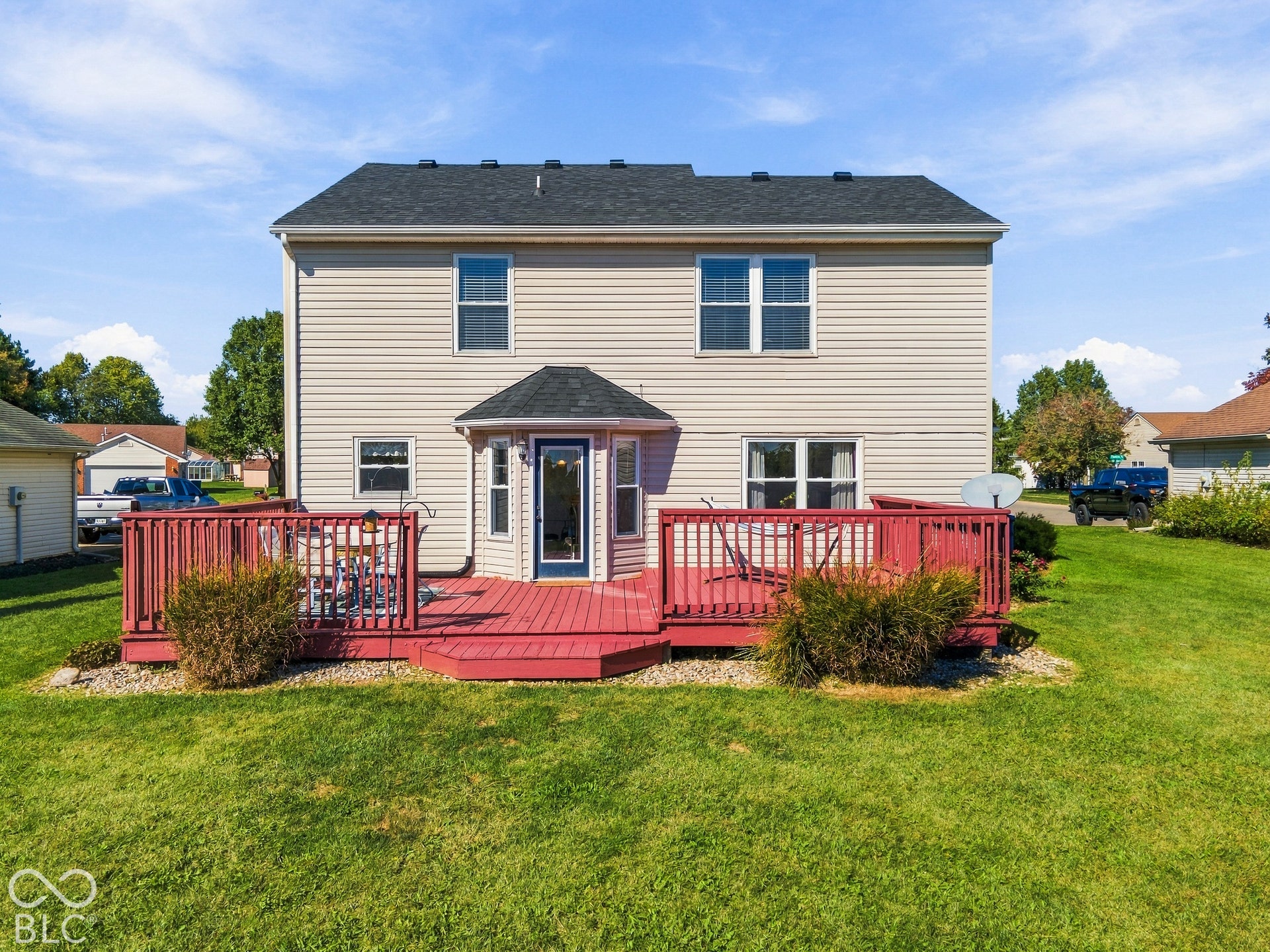 Expansive backyard featuring a large wooden deck with red staining, ample green lawn, and a two-story exterior with light-colored siding and a dark shingle roof