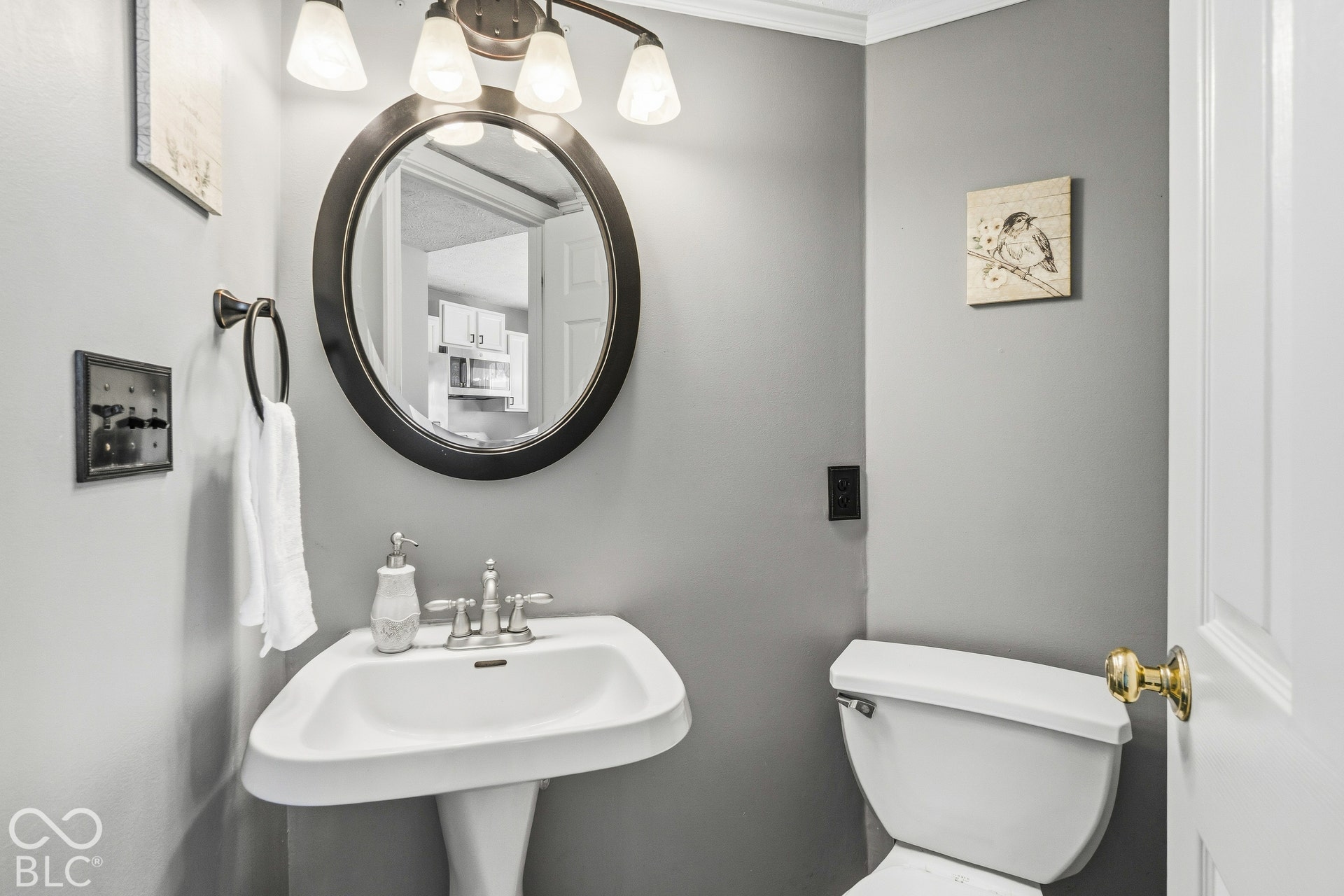Pedestal sink with stainless steel faucet, wall-mounted oval mirror, and a three-light vanity fixture