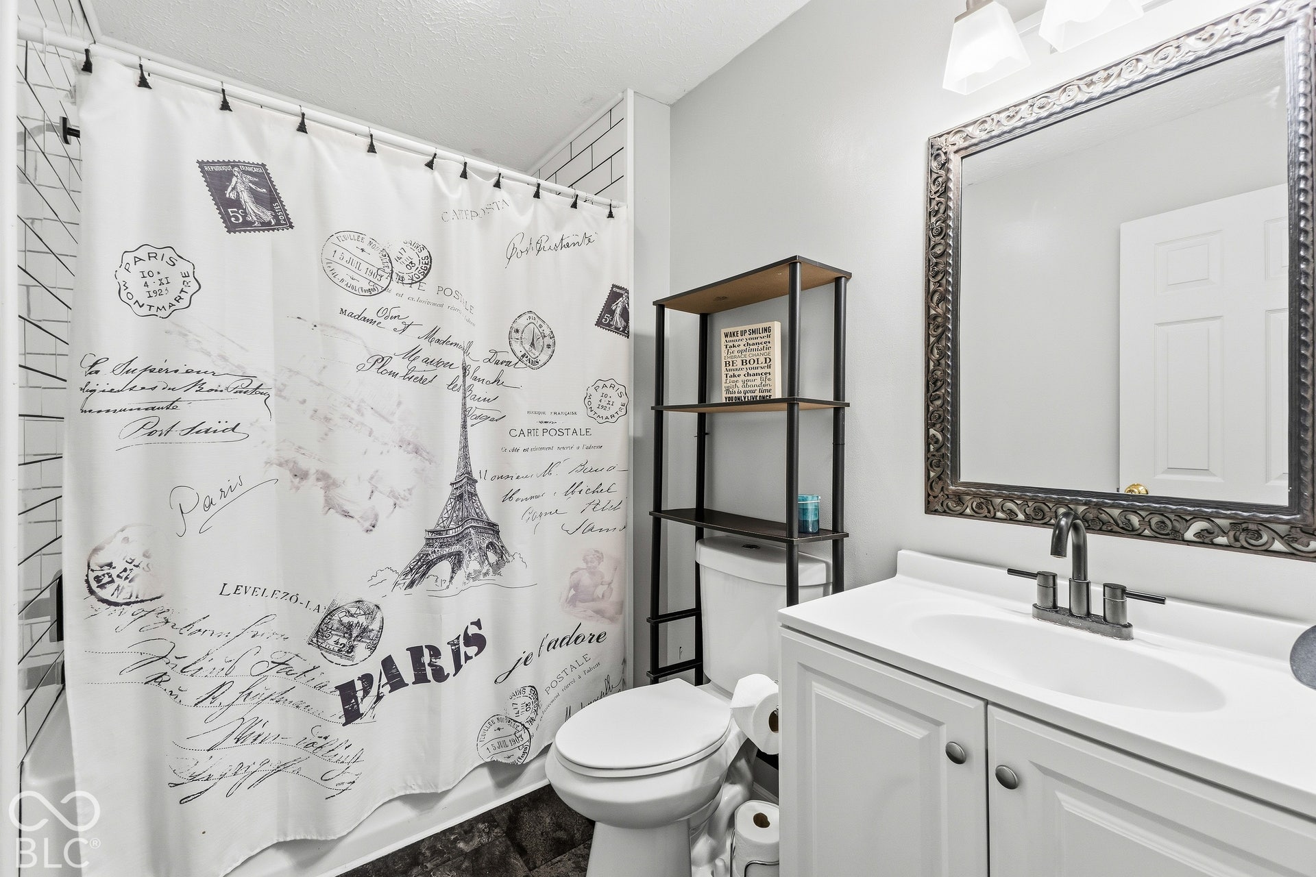 White subway tile shower surround, white vanity cabinet, single basin sink, and a decorative framed mirror