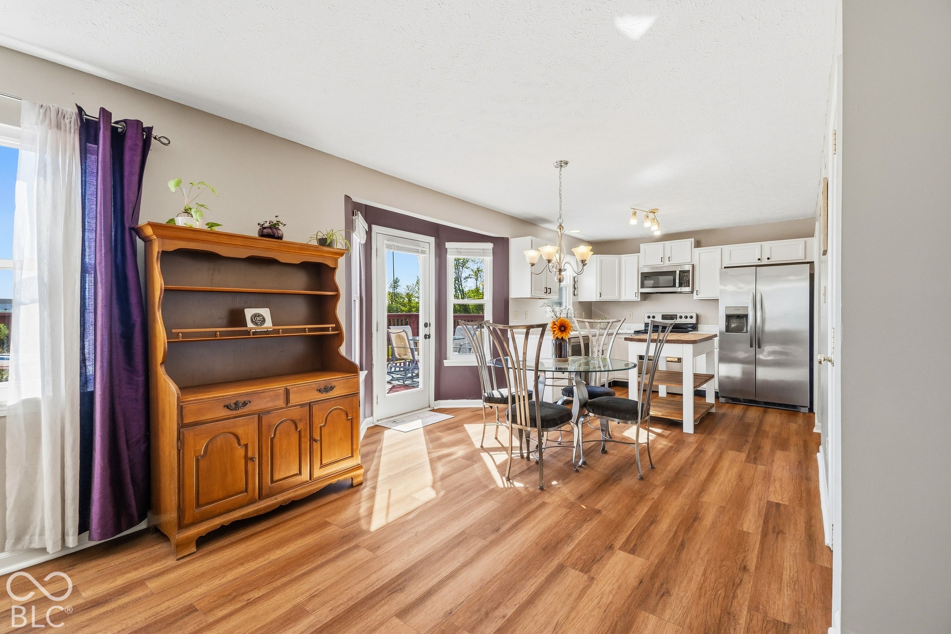 Open-concept living area with wood-finish flooring, white cabinetry, stainless steel appliances, and a glass-paneled door