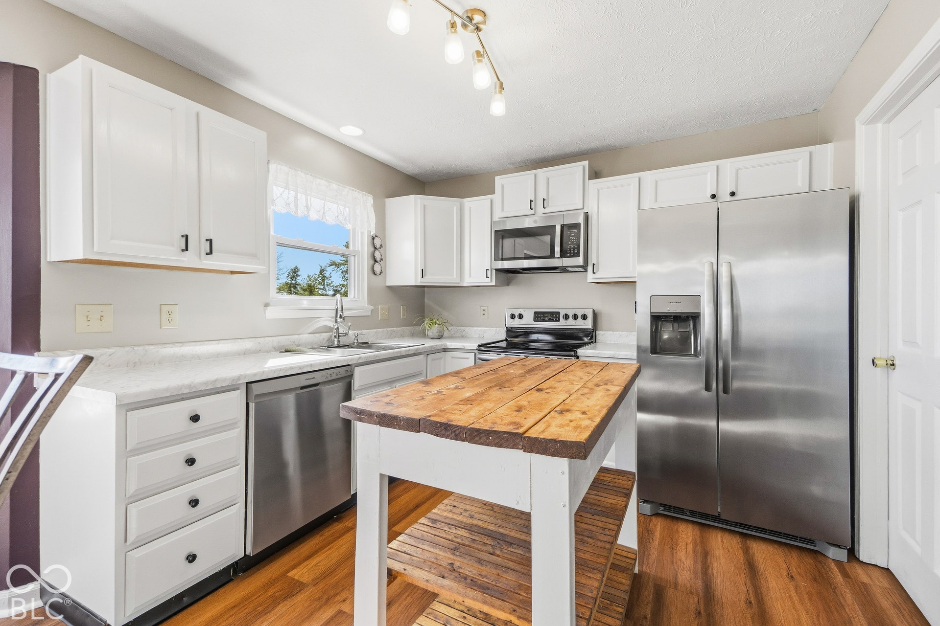 White cabinetry, stainless steel appliances, wood-finish flooring, light-toned countertops, and a wood-top island with shelving