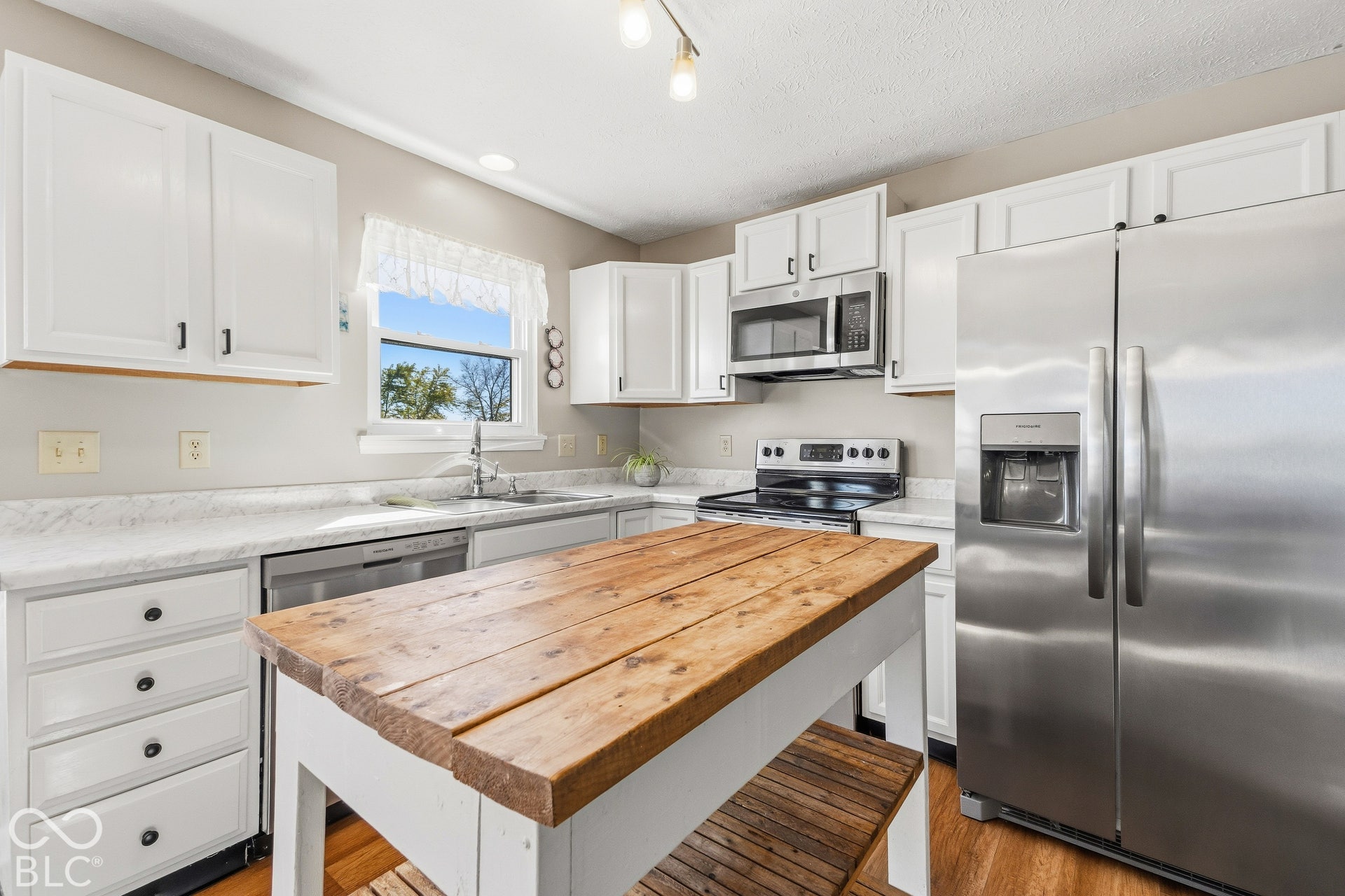 White cabinetry with dark hardware, stainless steel appliances, wood-finish flooring, and a central wood-top island