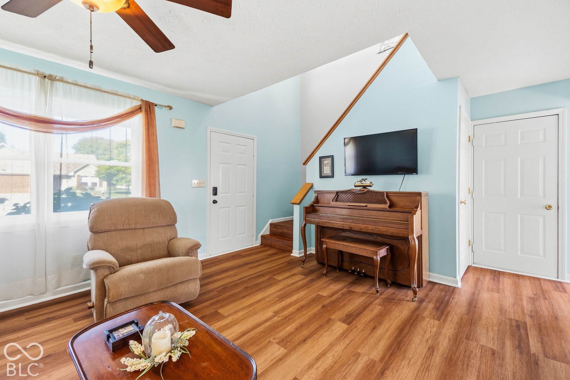 Living space with wood-finish flooring, a white paneled door, and a ceiling fan with integrated lighting