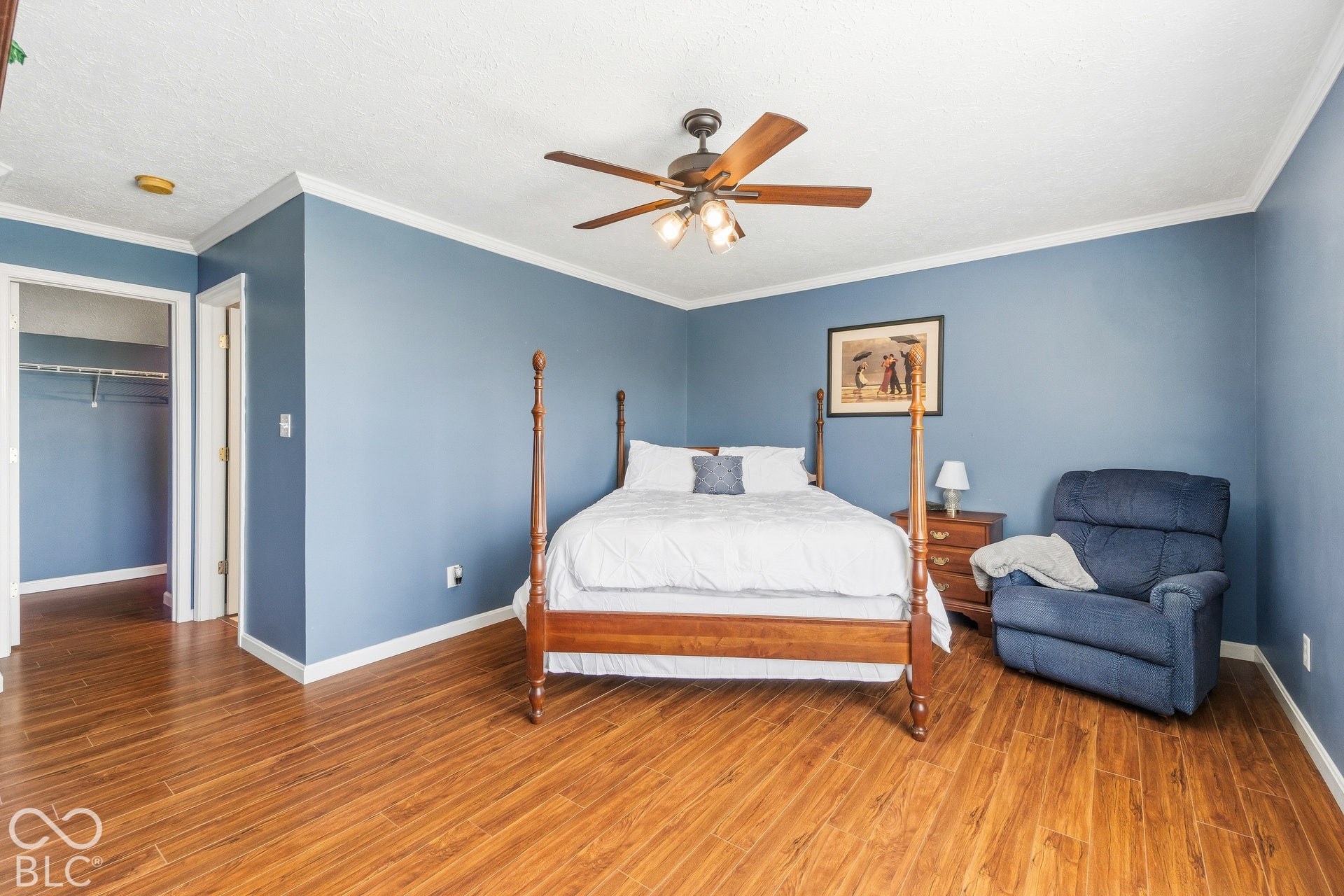 Wood-finish flooring, ceiling fan with integrated lighting, crown molding, and recessed closet with shelving