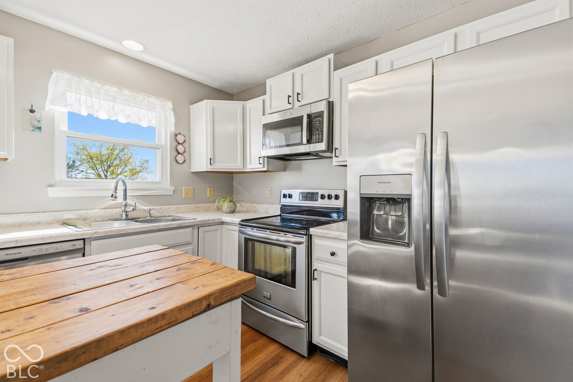 White cabinetry with dark hardware, stainless steel appliances, light-toned countertops, and wood-finish flooring