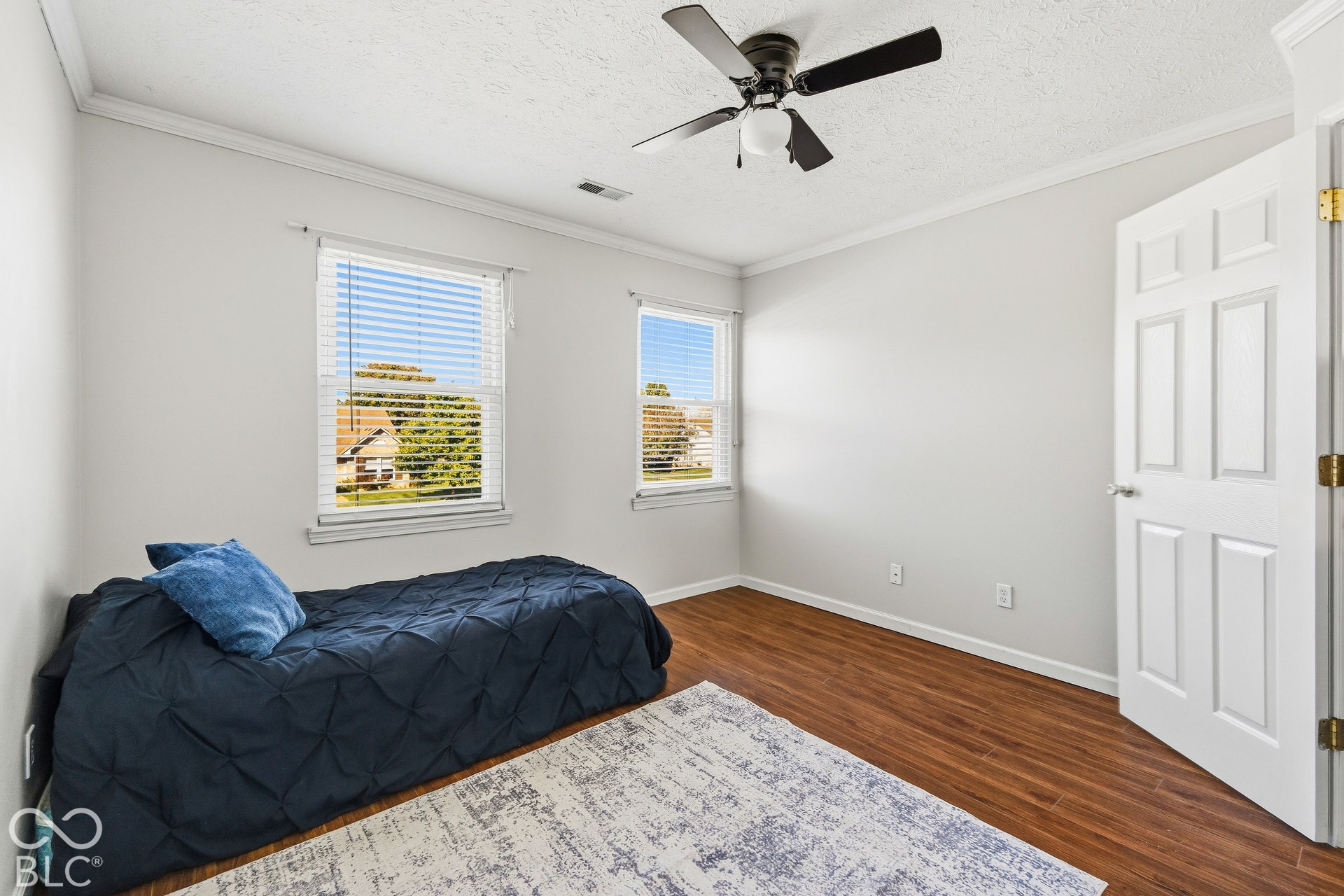 Wood-finish flooring, two windows with blinds, ceiling fan with integrated lighting, paneled door, and crown molding