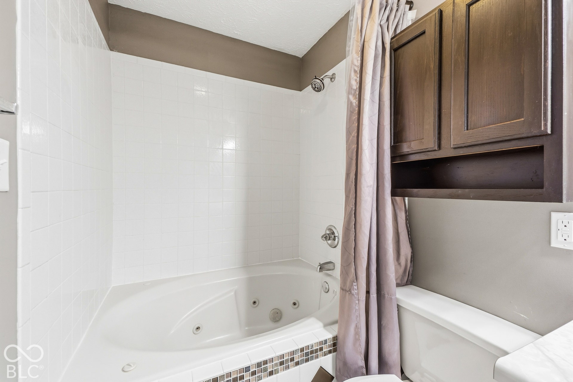 Built-in jetted tub with white subway tile surround, mosaic accent tile, and a wall-mounted showerhead