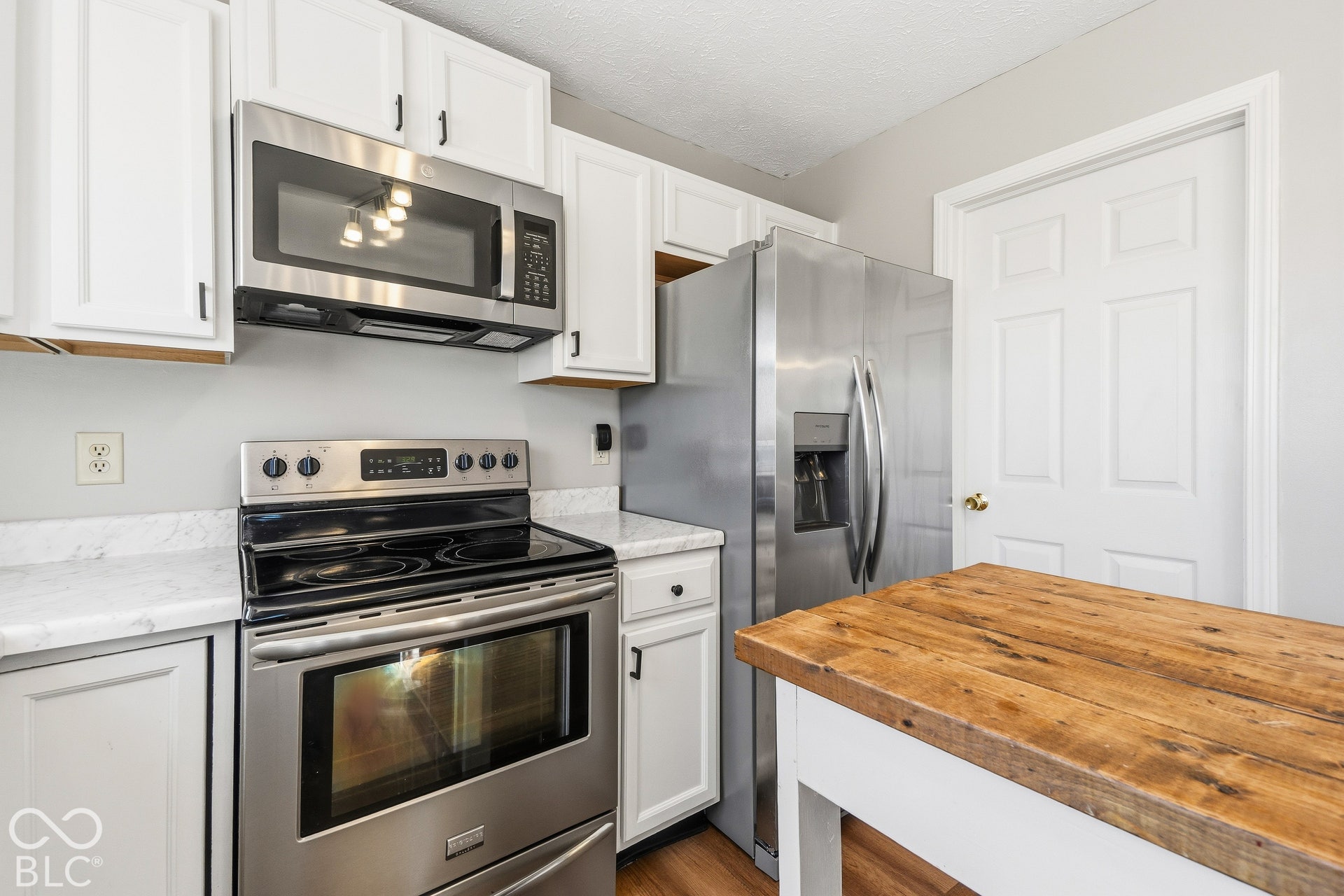 Stainless steel appliances, white cabinetry, wood-finish flooring, white countertops, and a wood-finish island