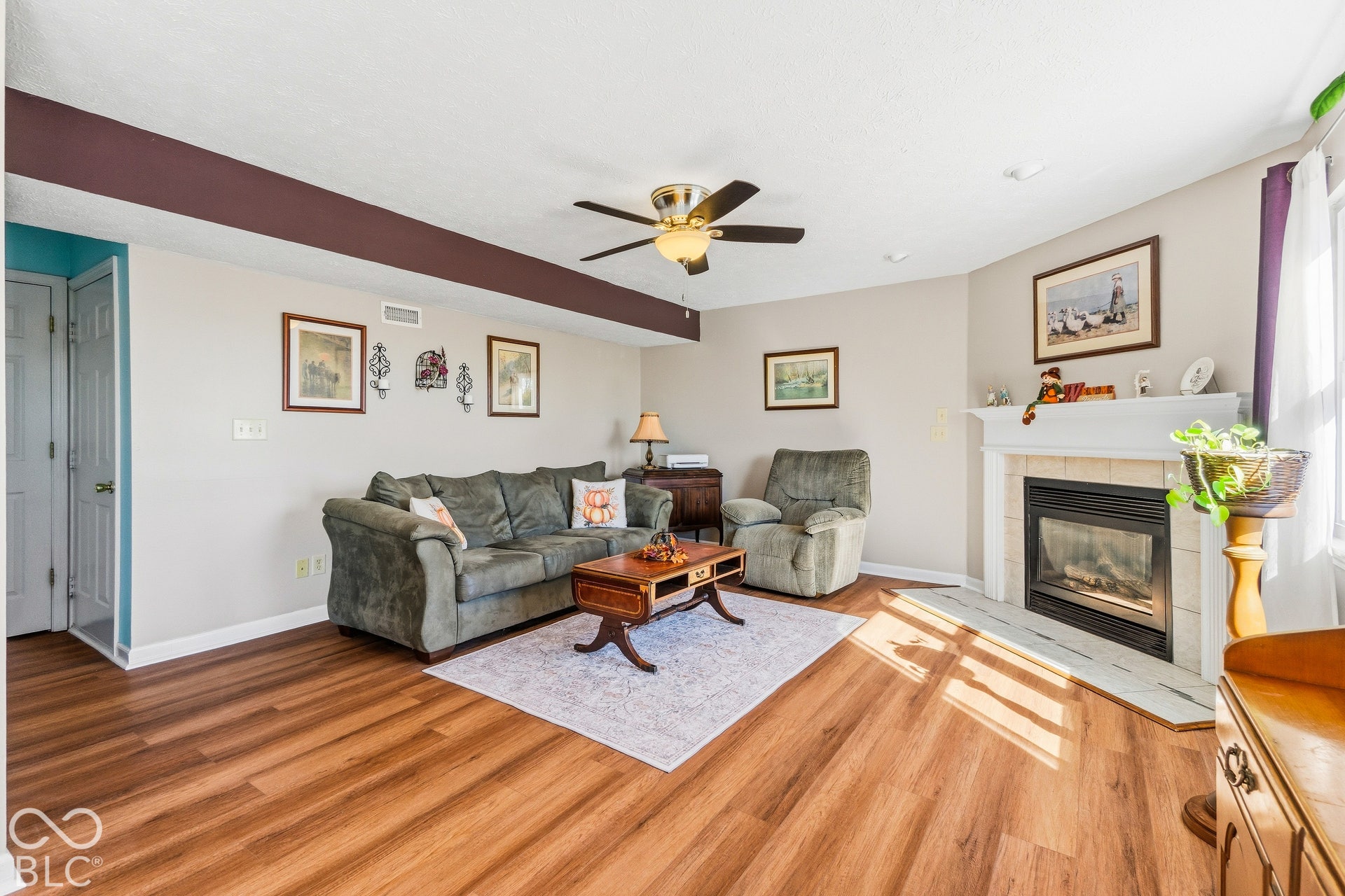 Wood-finish flooring throughout, ceiling fan with integrated lighting, and a fireplace with a tile hearth and mantle