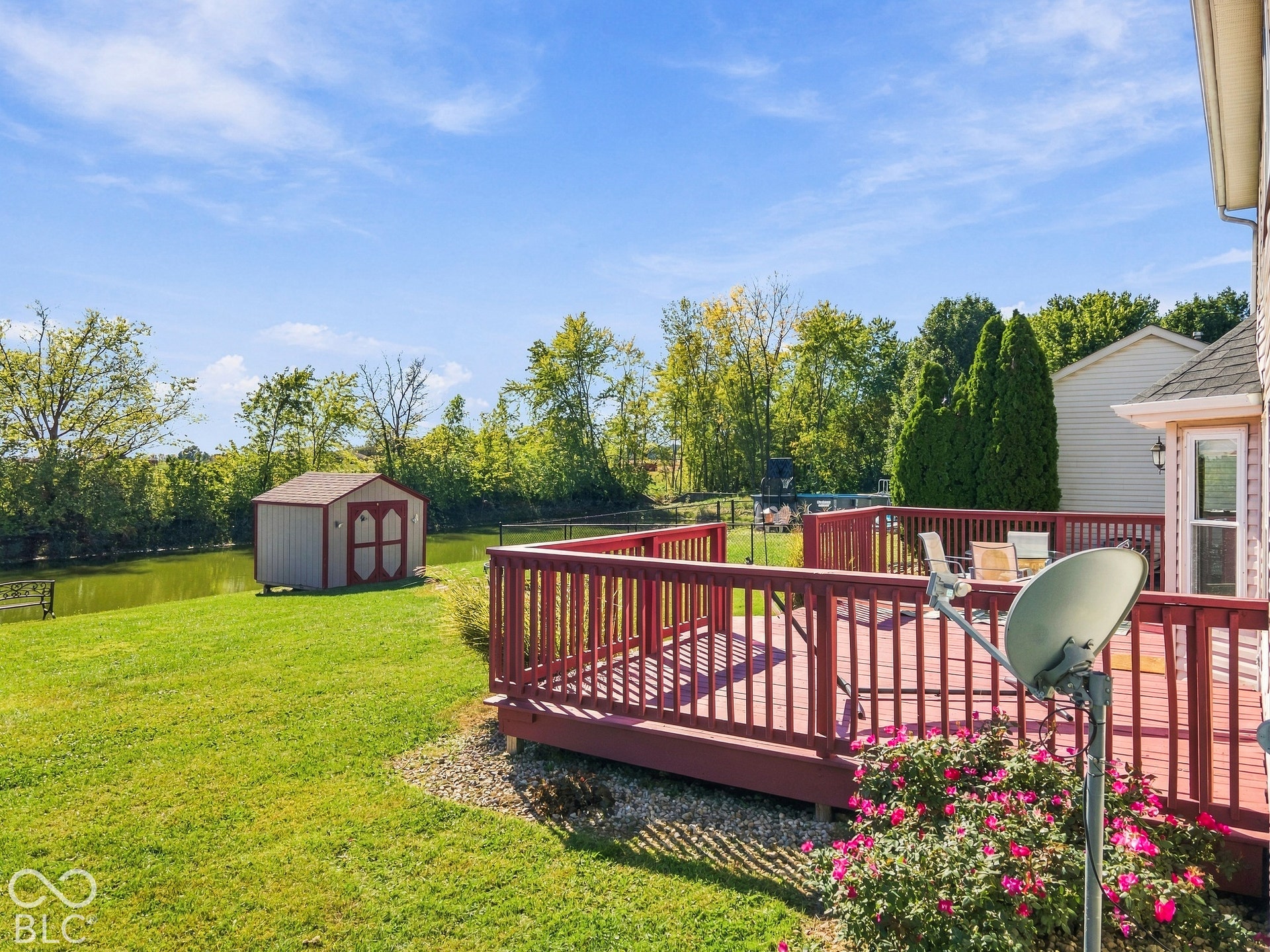 Expansive backyard featuring a red wood-finish deck, mature trees, a storage shed, and a water feature