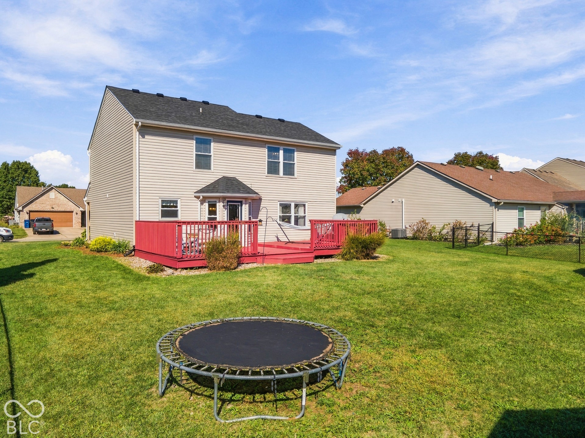 Expansive rear lawn with a red-painted wood deck, vinyl siding exterior, and a dark shingle roof