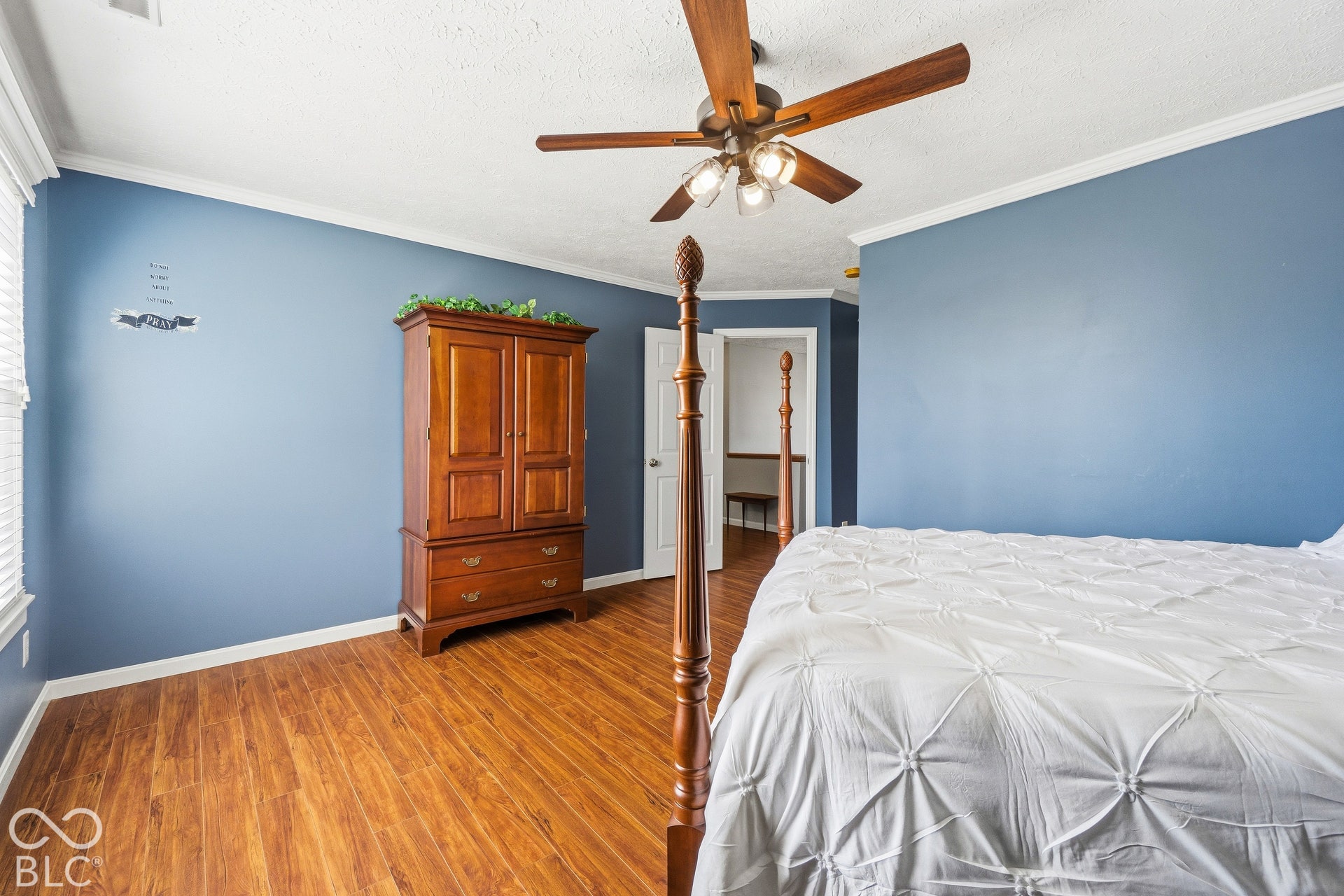 Wood-finish flooring, ceiling fan with integrated lighting, crown molding, and blue painted walls