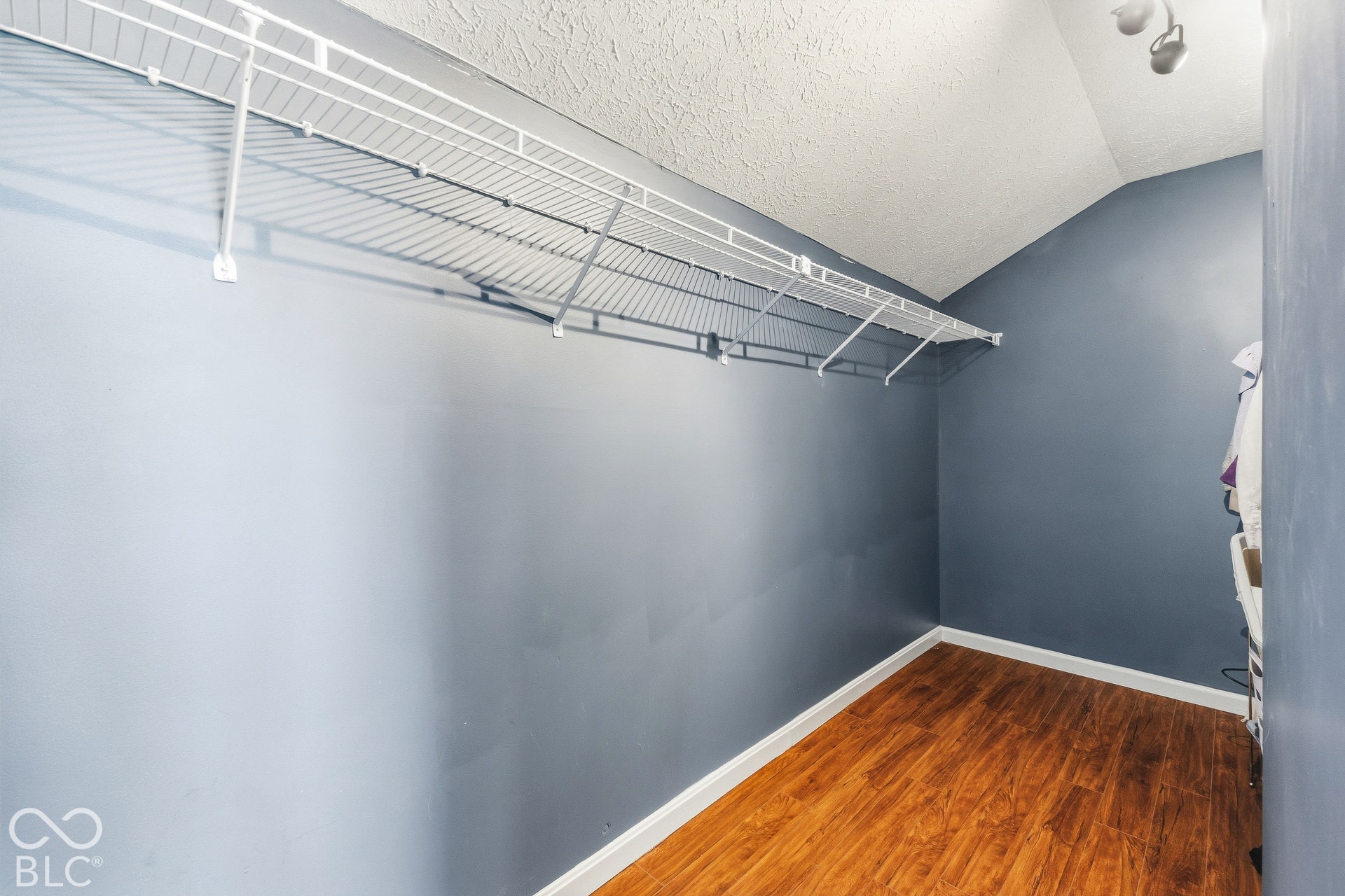 Wood-finish flooring with white baseboards, wire shelving, and track lighting