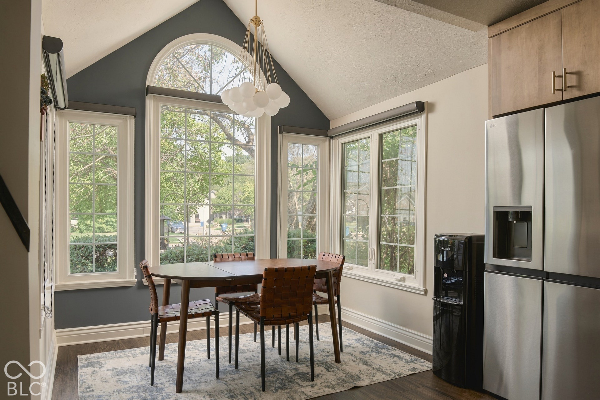 Vaulted ceiling with an arched window, a contemporary chandelier, and wood-finish flooring