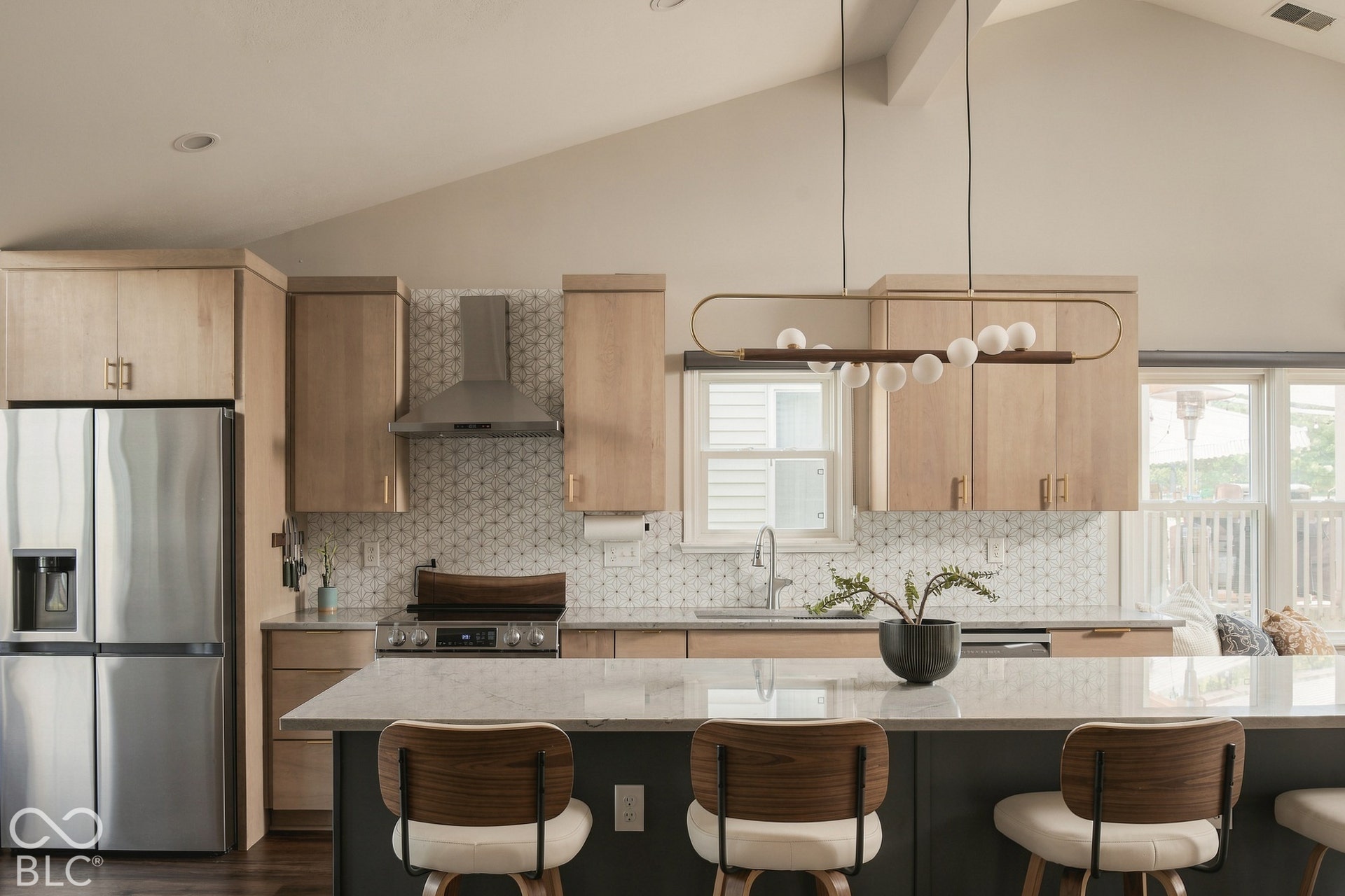 Vaulted ceiling, wood-finish cabinetry, stainless steel appliances, stone countertops, and a decorative light fixture