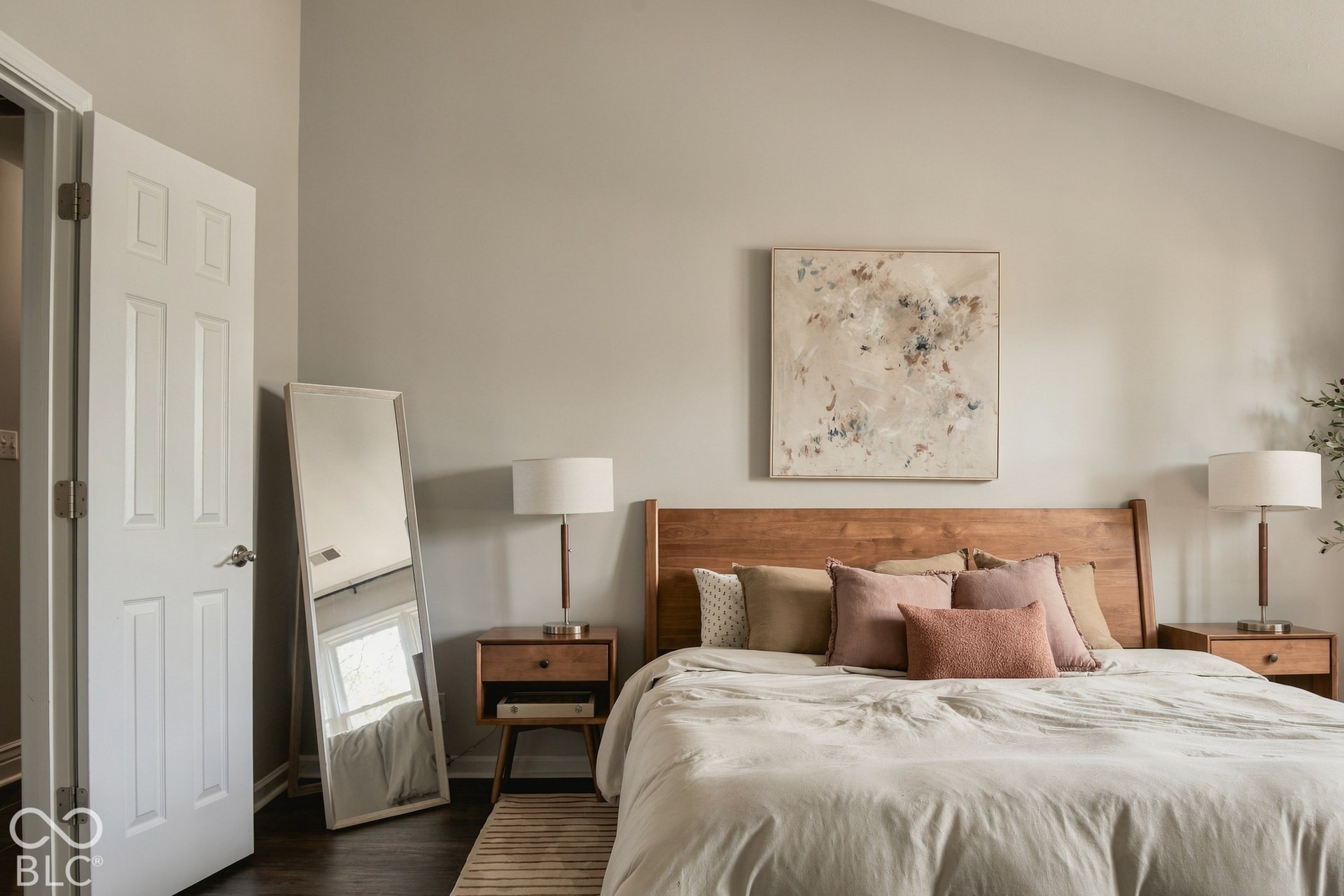 Vaulted ceiling accentuates the spaciousness of this bedroom with dark wood-finish flooring and light-toned walls