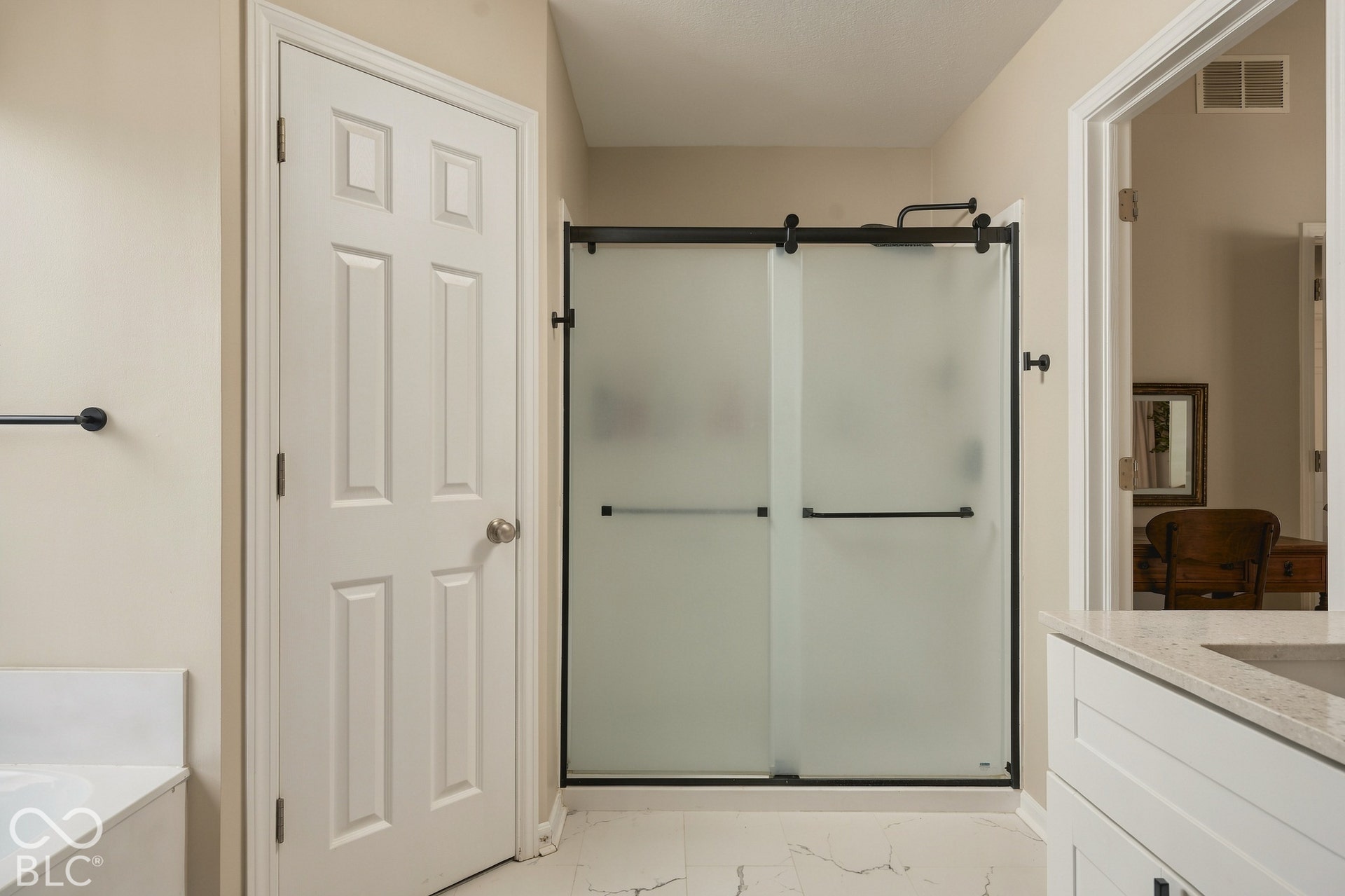 Frosted glass shower enclosure with matte black hardware, white paneled door, and light-toned flooring
