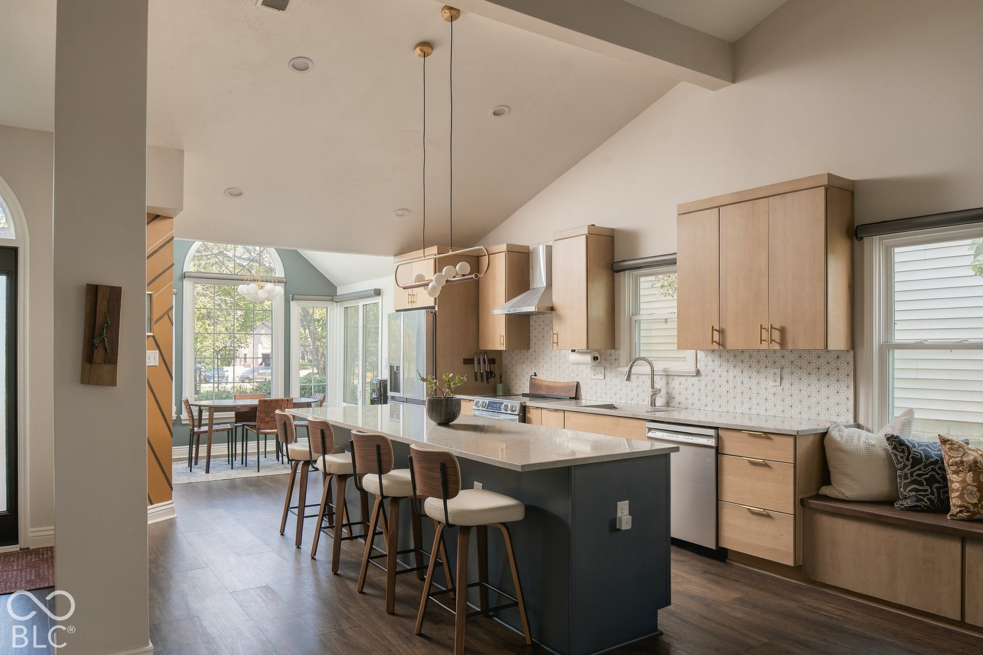 Vaulted ceiling kitchen featuring a large center island, wood-finish flooring, light-toned cabinetry, and a built-in window seat